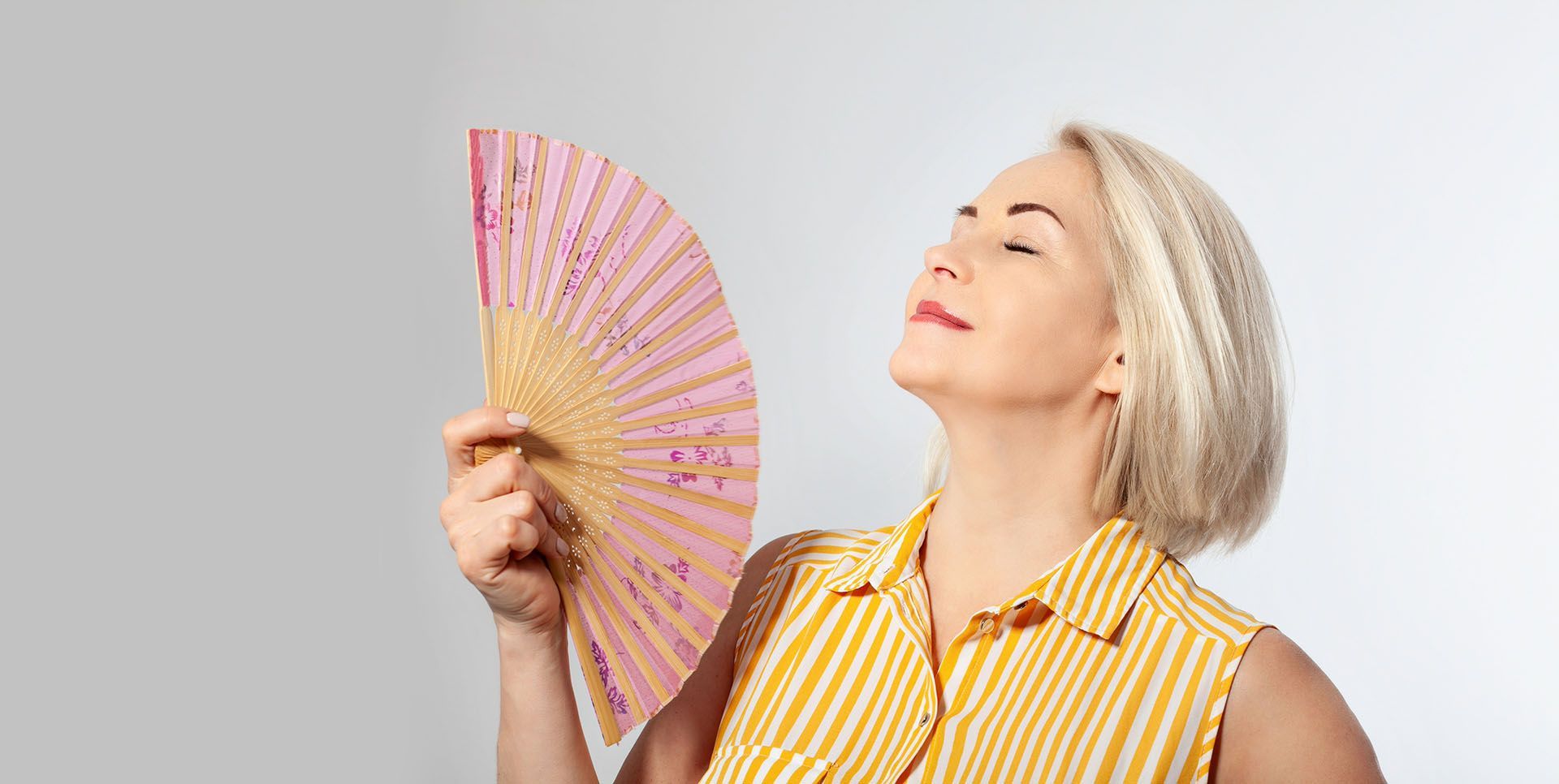 A woman in a yellow and white striped shirt is holding a pink fan.