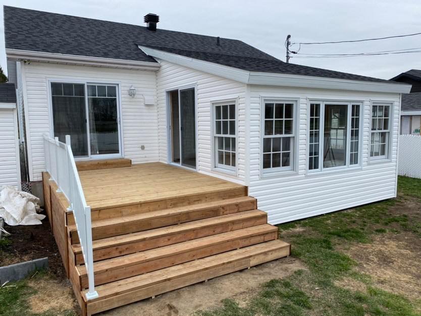 une maison blanche avec une terrasse en bois et des escaliers devant.