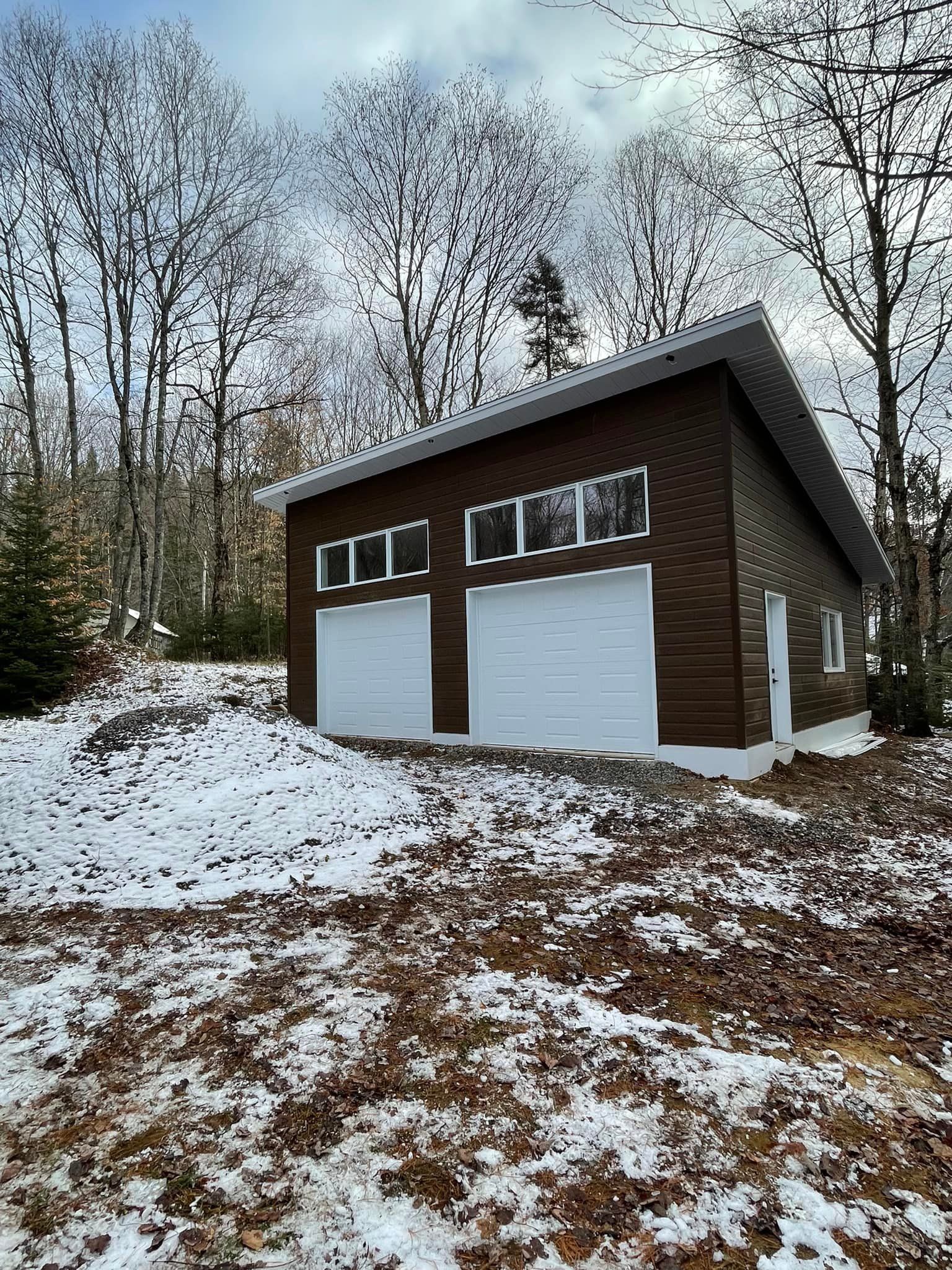 un garage avec deux portes de garage se trouve au sommet d une colline enneigée.