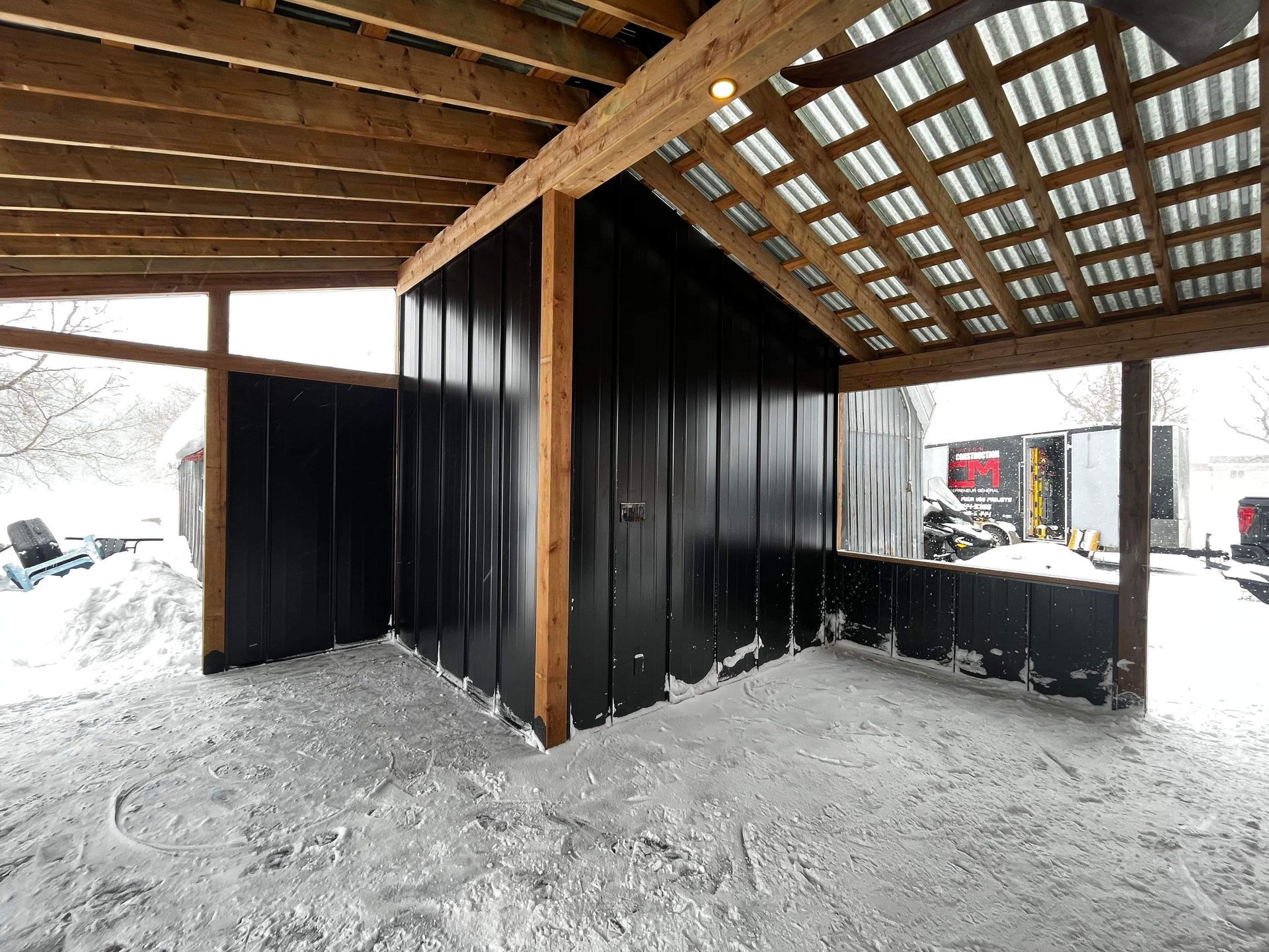 Un bâtiment aux murs noirs et au toit en bois est recouvert de neige.