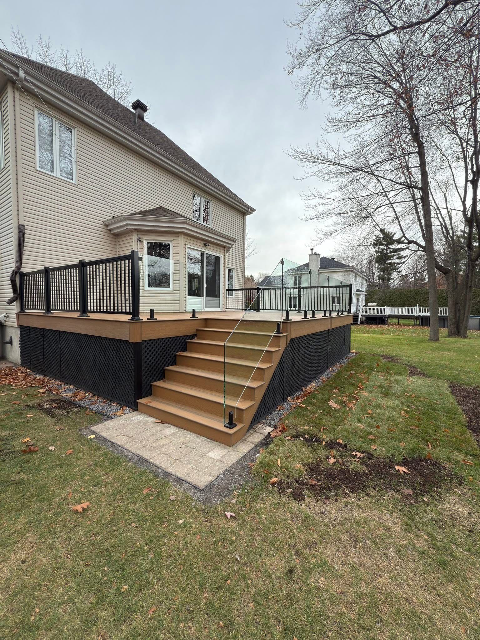 Une maison beige avec une nouvelle terrasse en composite dotée de rambardes noires et de plinthes en treillis, accessible par un large escalier marron.