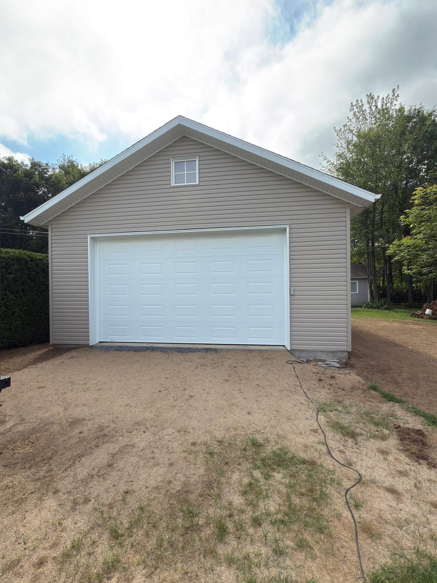 Un garage indépendant beige avec une porte sectionnelle blanche et une petite fenêtre, situé sur une allée de gravier.
