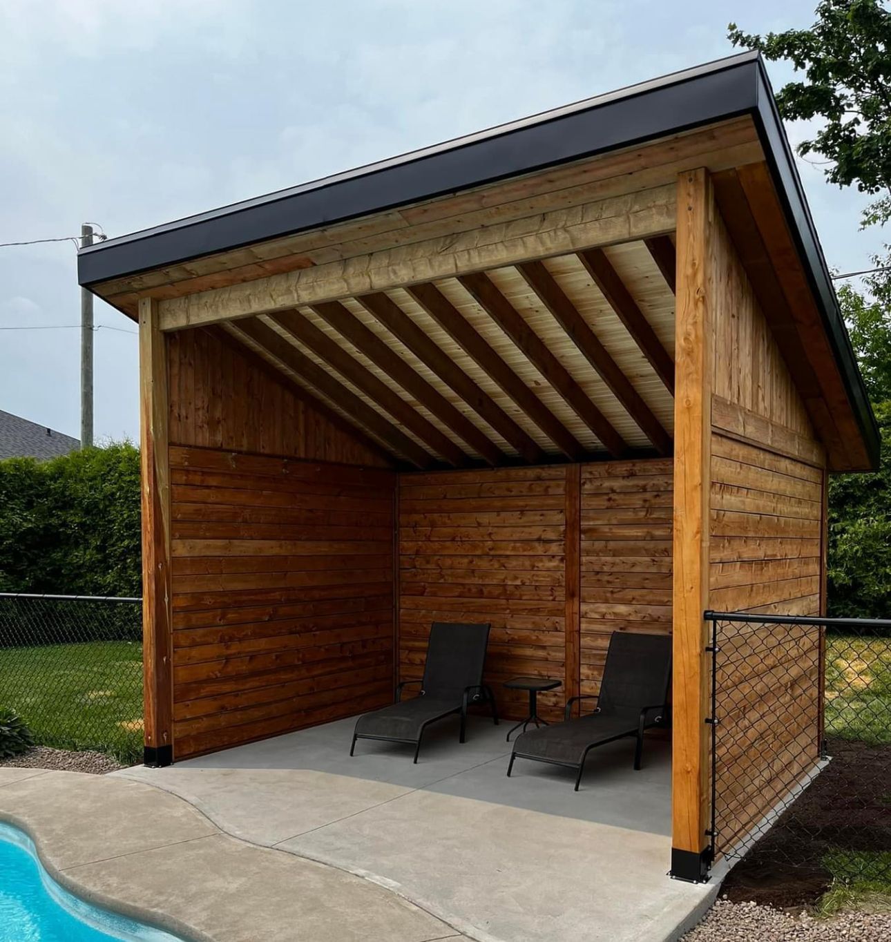 Un abri en bois avec des chaises en dessous, à côté d'une piscine