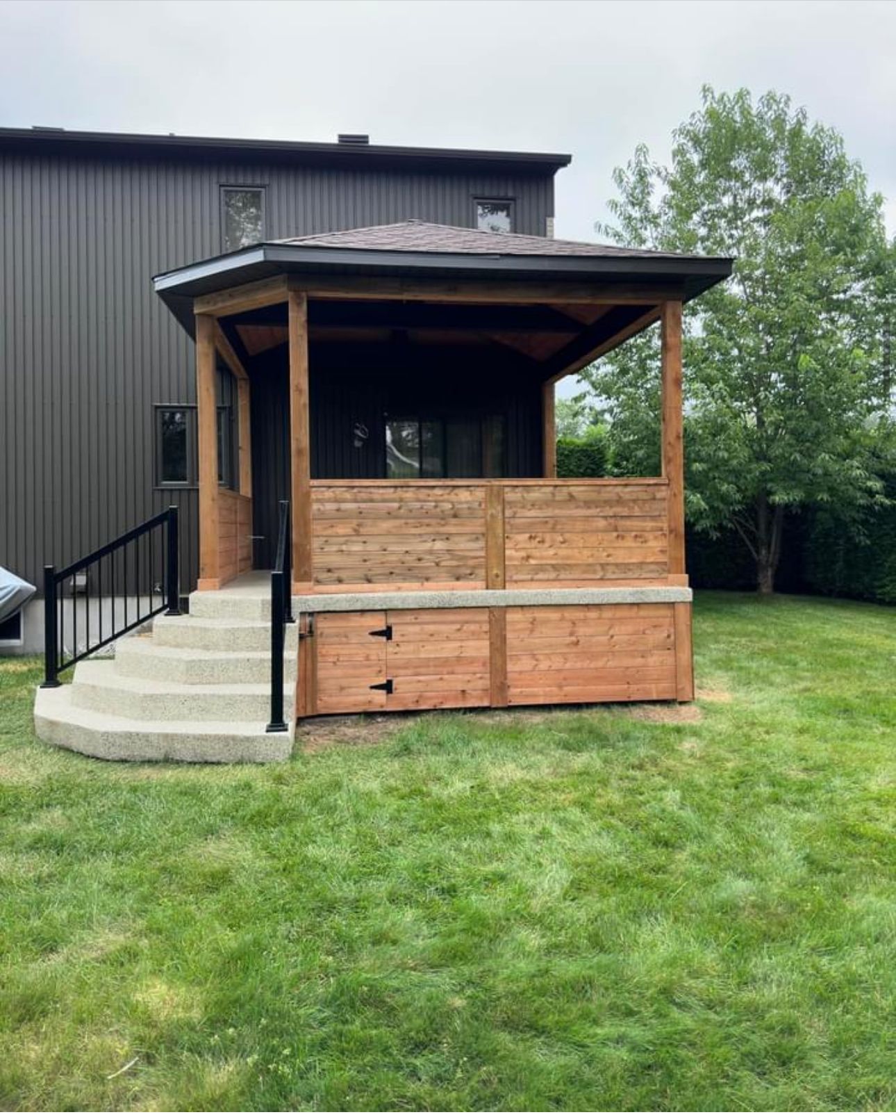 Un belvédère en bois se trouve au milieu d'une cour verdoyante.