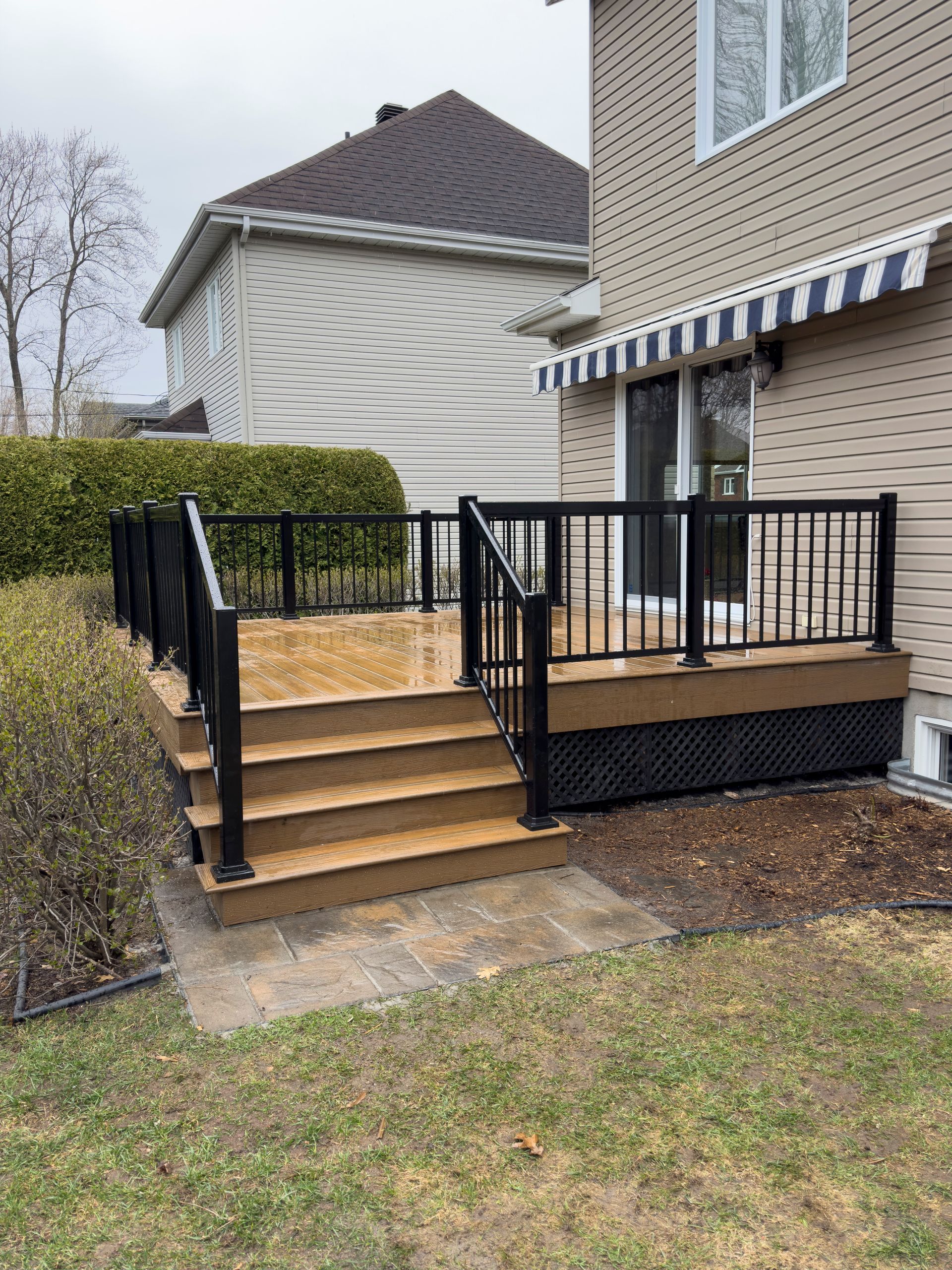 Une terrasse en bois avec des escaliers et une balustrade noire devant une maison.