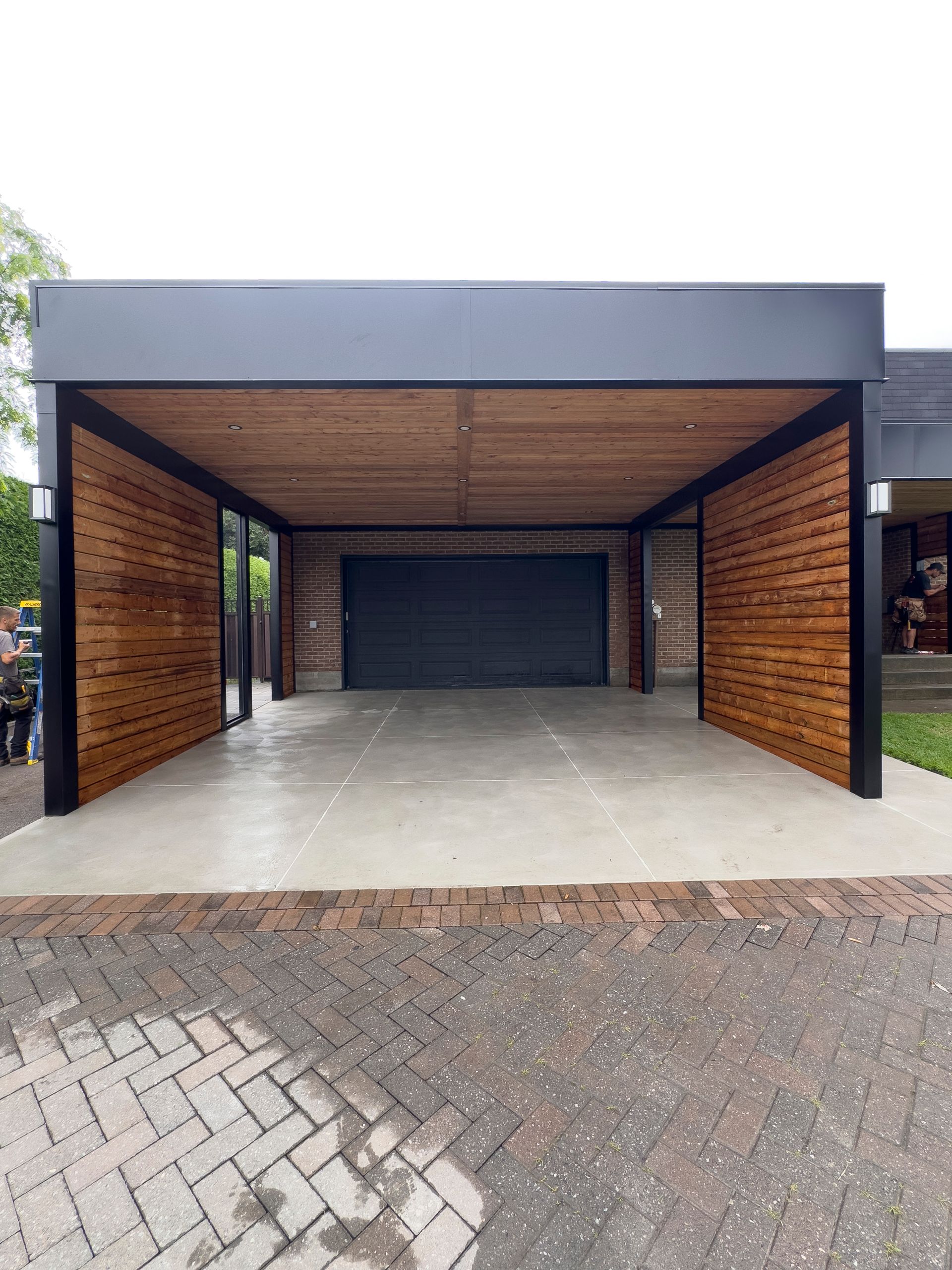 Un abri d'auto avec un toit en bois et une allée en briques devant une maison.