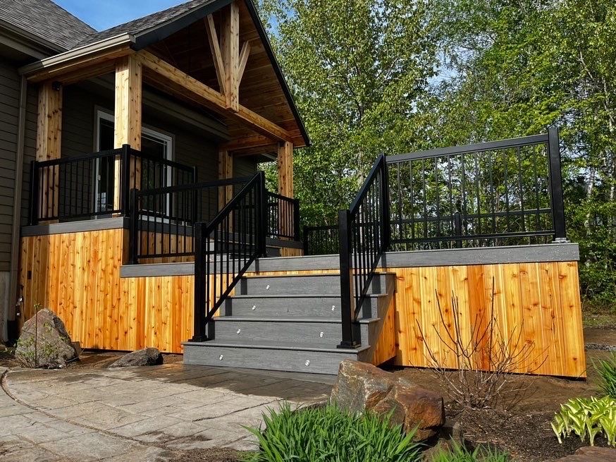 Porche et marches en bois avec balustrade noire ; maison et arbres en arrière-plan.