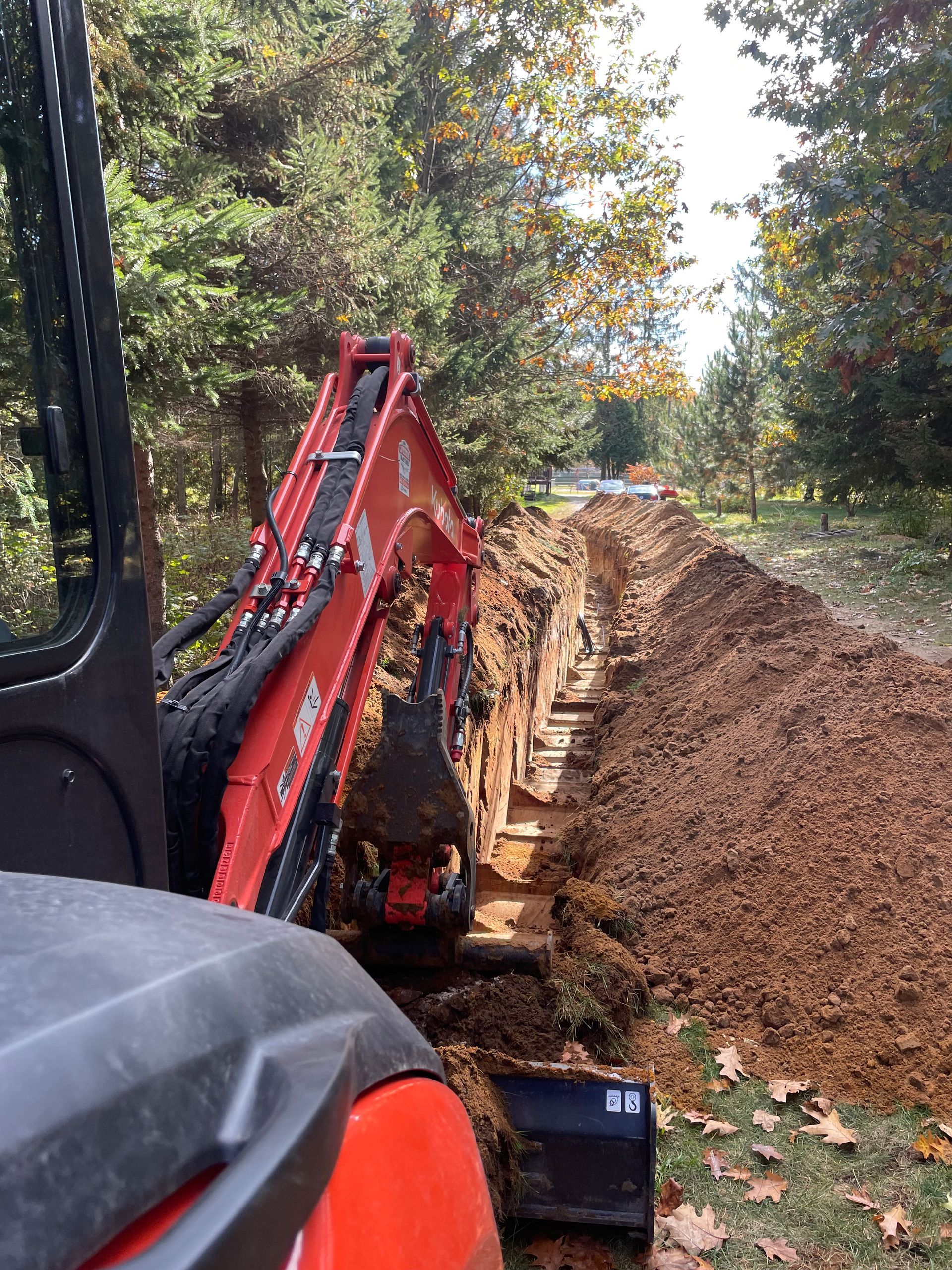 une excavatrice rouge et noire creuse une tranchée dans la terre.
