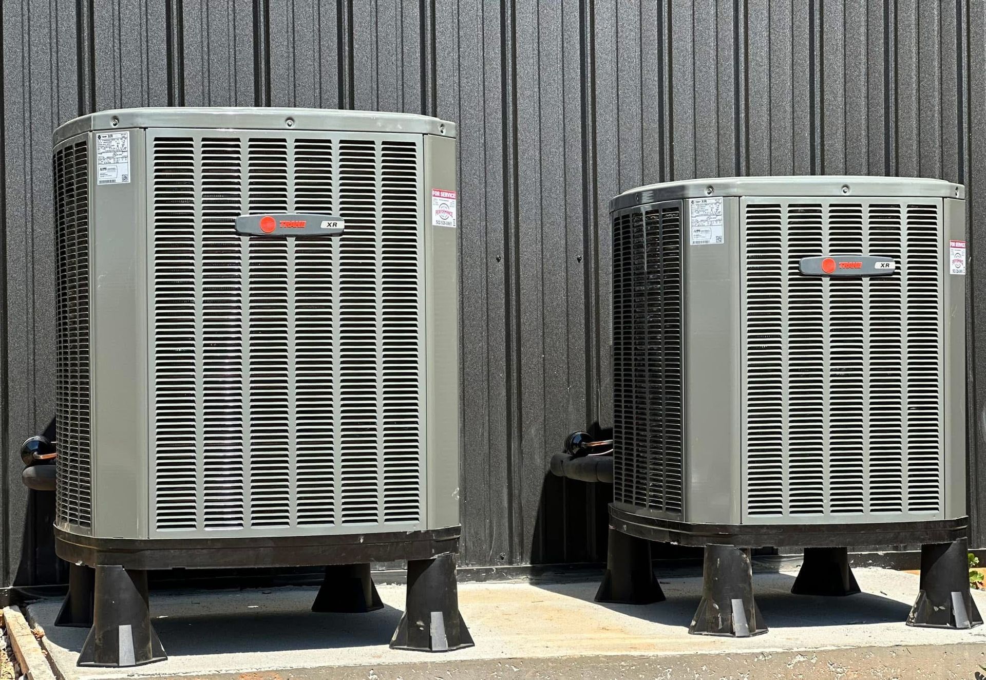 Two air conditioners are sitting next to each other in front of a building.