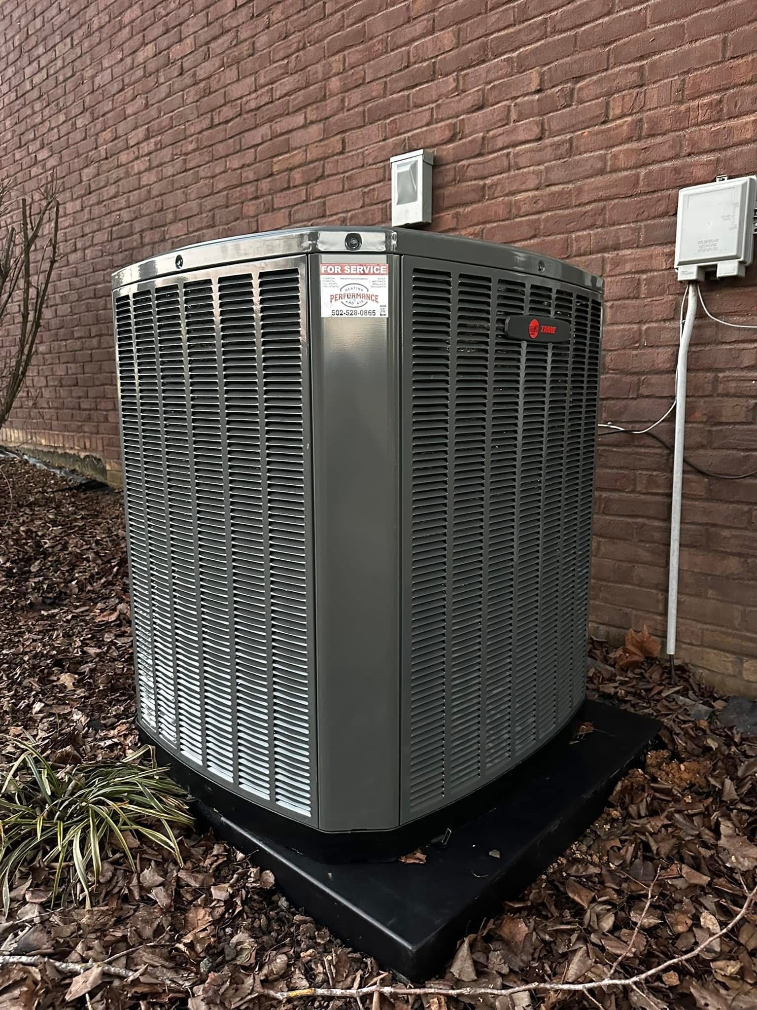 A large air conditioner is sitting outside of a brick building.