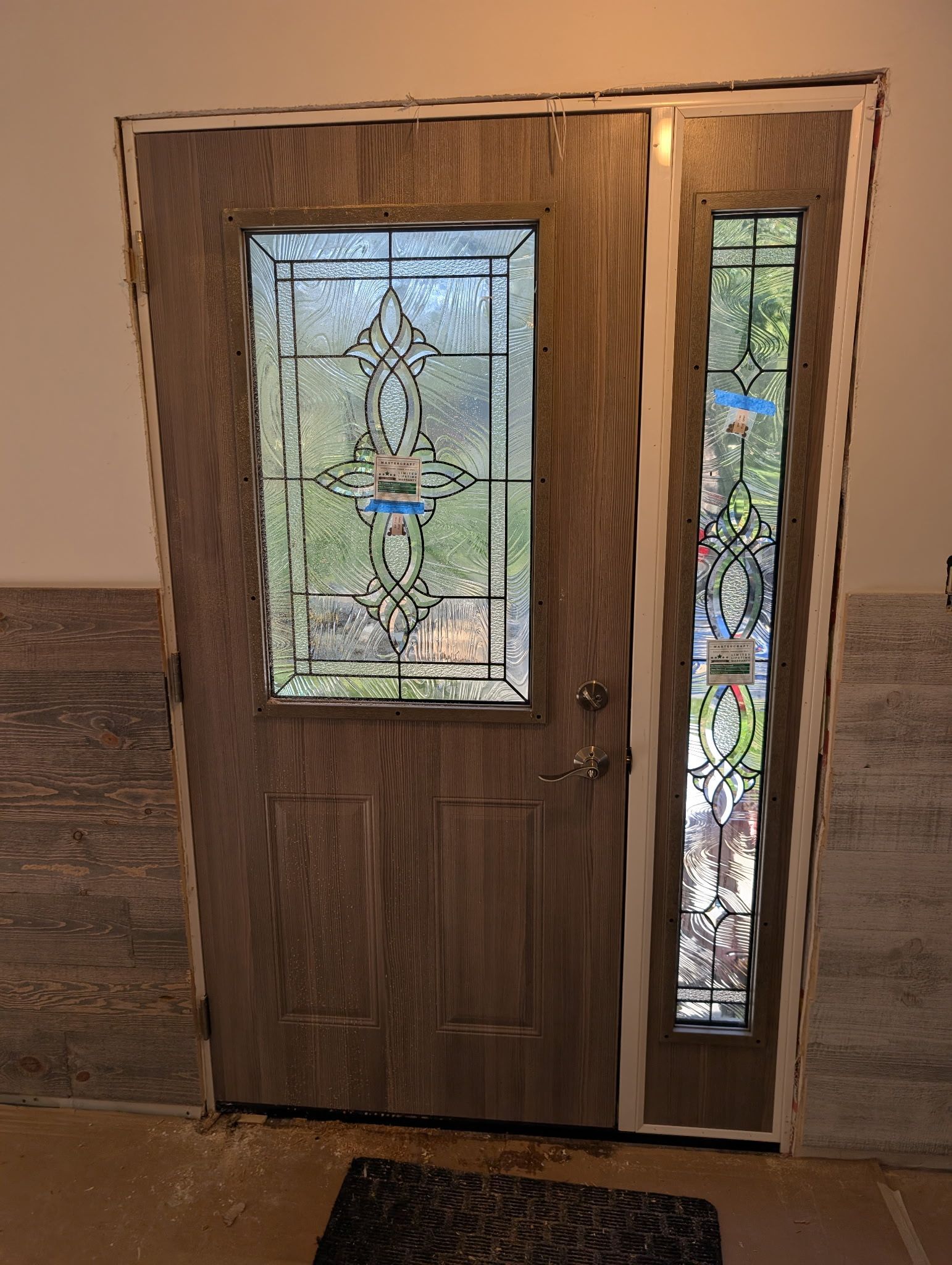 Two construction workers installing siding on a building, both wearing orange shirts and tool belts.