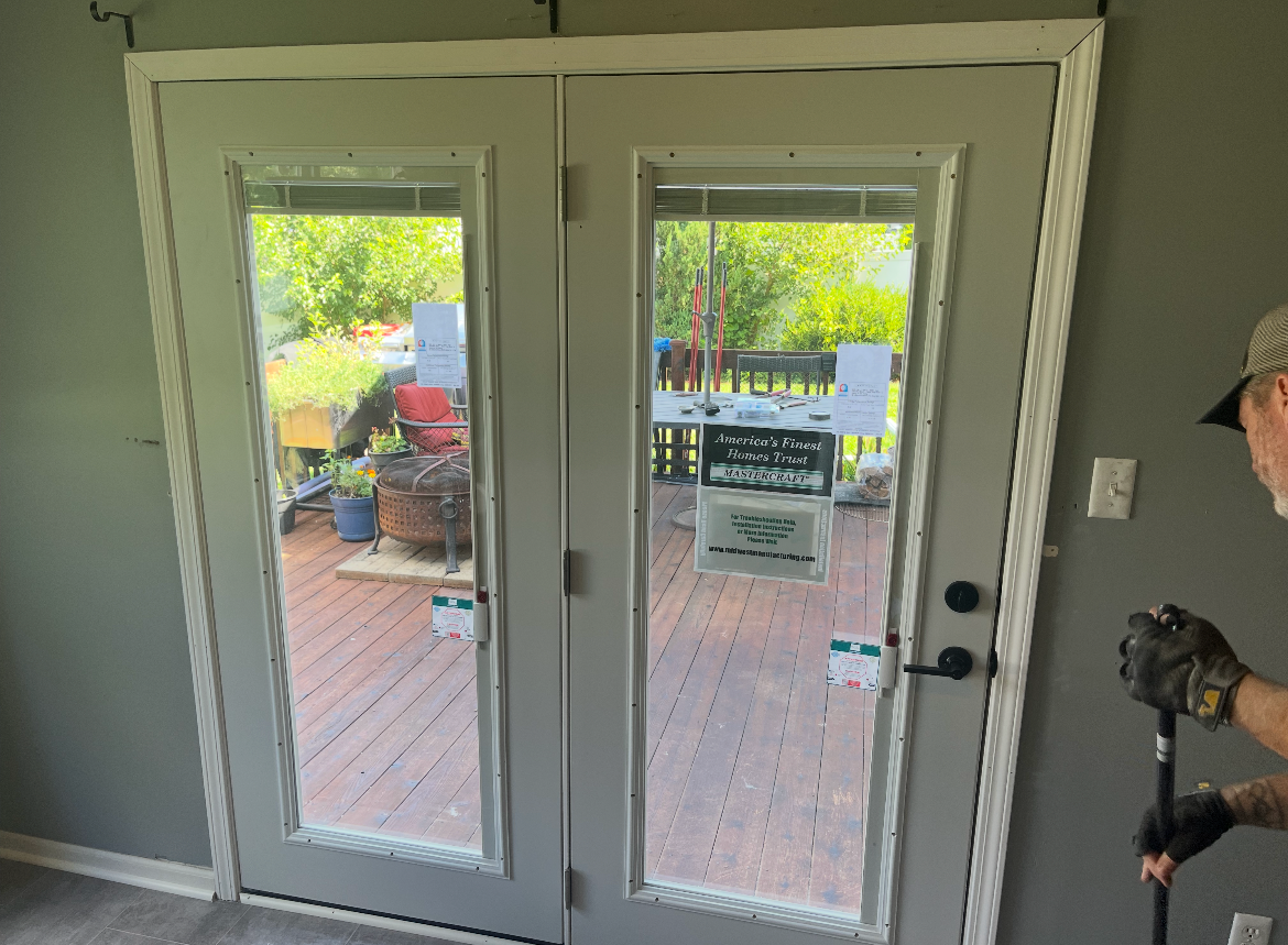 Beige gutters on a house with gray siding and a black shingled roof, against a blue sky.