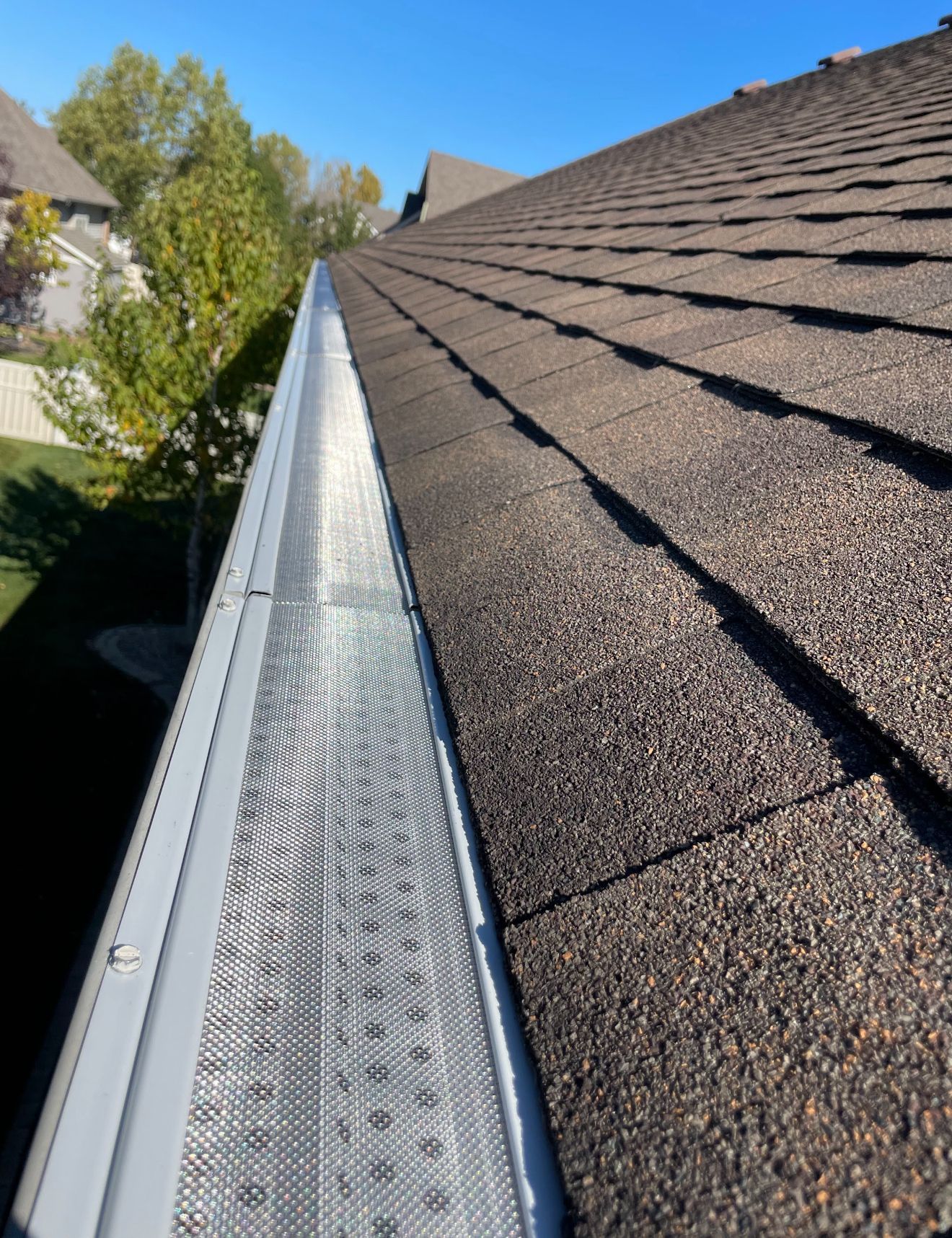 Man power washing a shingled roof while standing on a ladder under a partly cloudy sky.