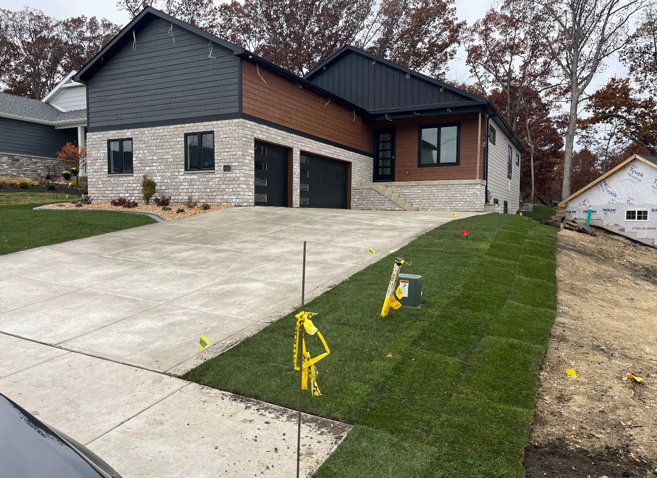 Roofer on a roof inspecting shingles, holding a ladder. Houses in the background, sunny day.