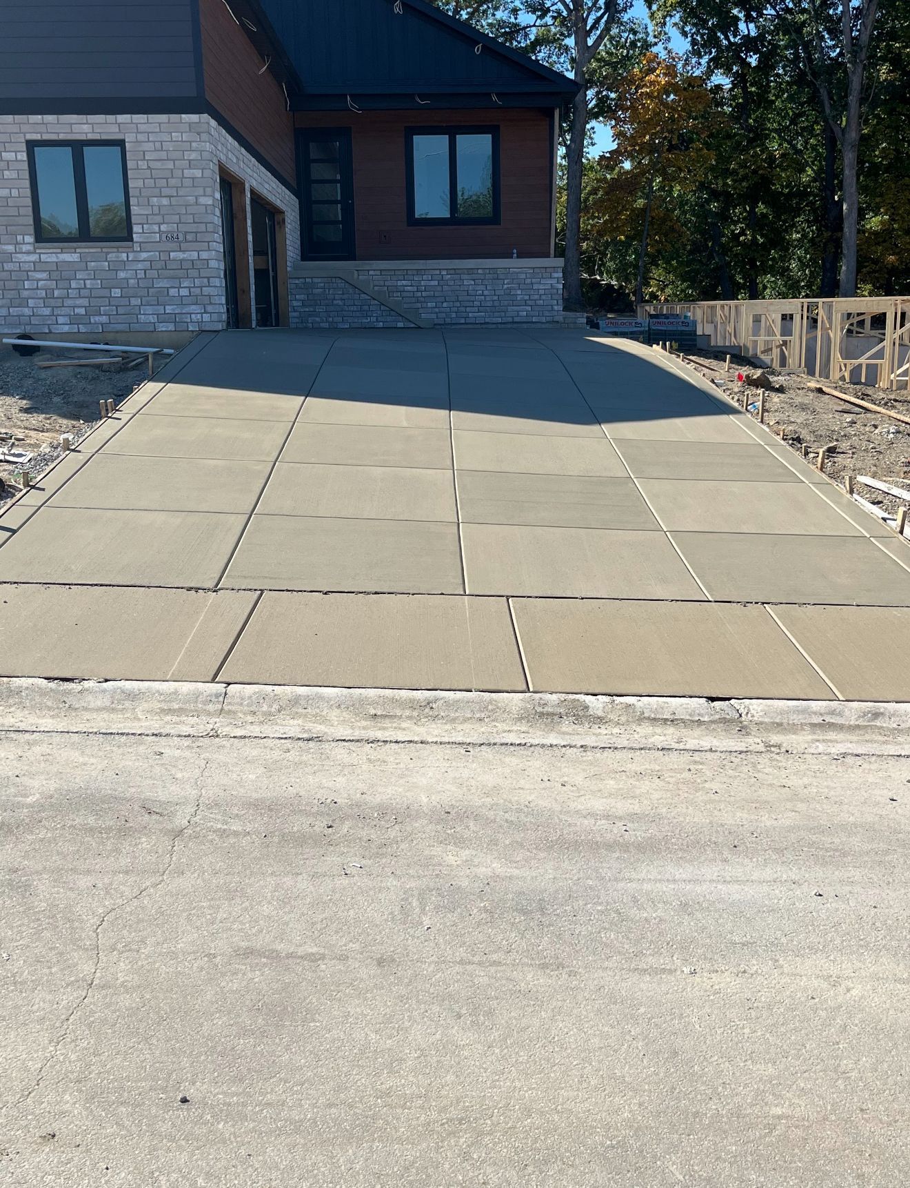 Two construction workers installing siding on a building, both wearing orange shirts and tool belts.