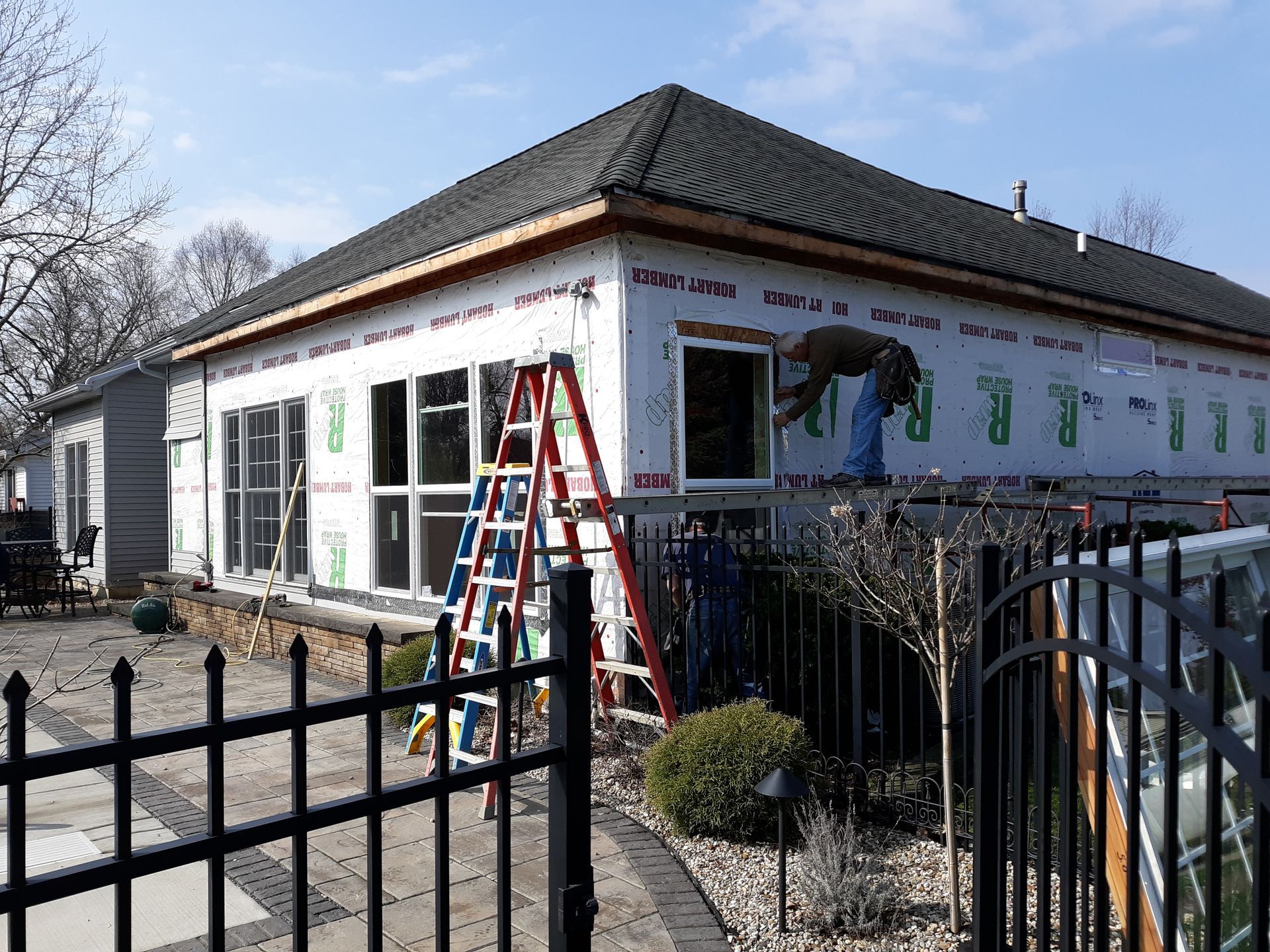Wooden deck with steps leading to a two-story house with cedar and gray siding, surrounded by trees.