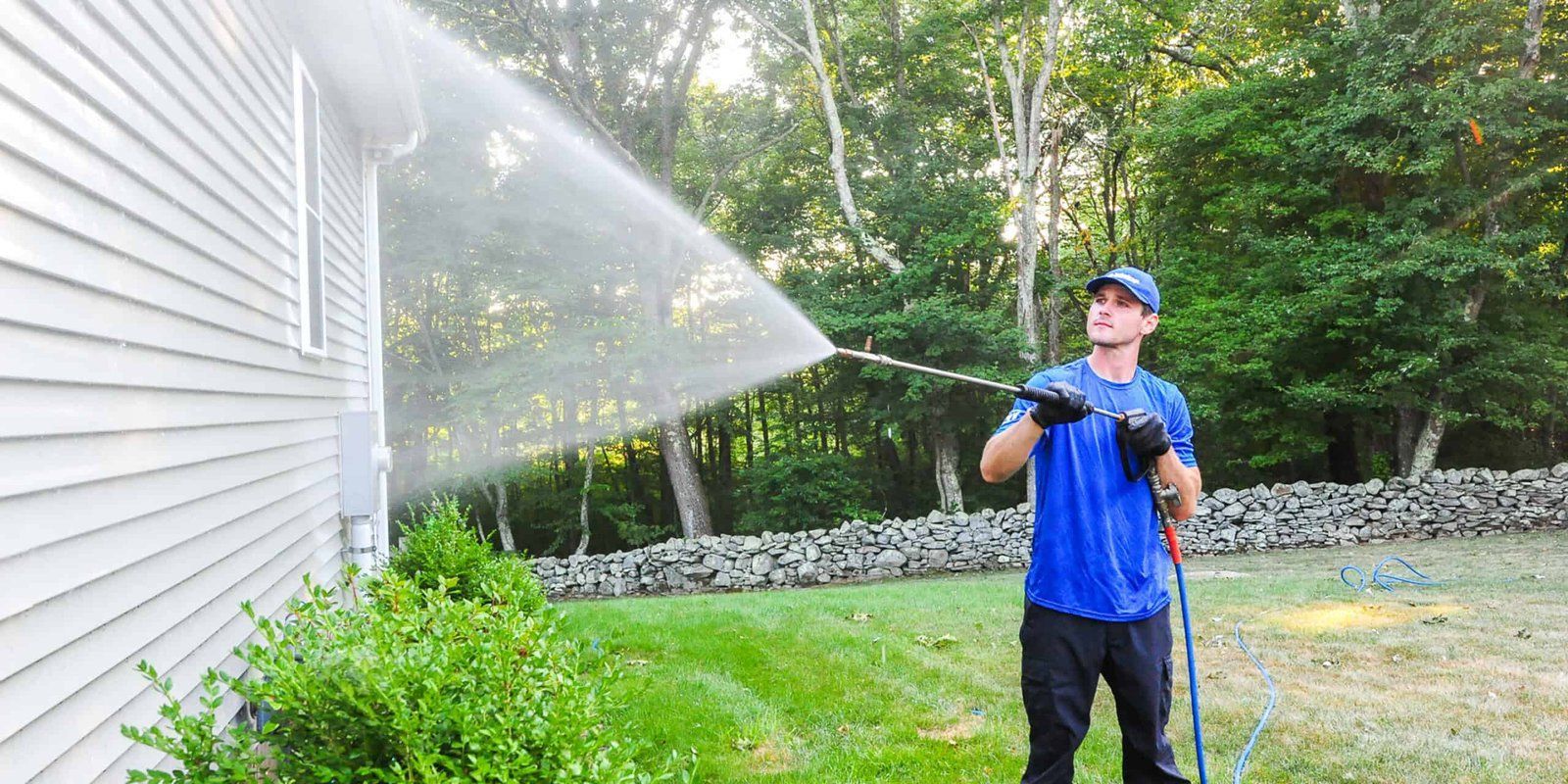A person power washing the side of a house, with water spraying.