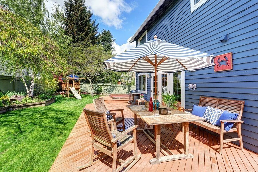 Blue house with wooden deck, patio furniture, striped umbrella, and green lawn.