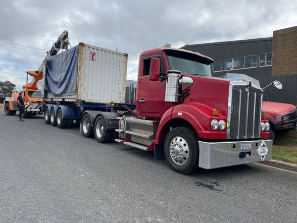 A red semi truck with a white container on the back is parked on the side of the road.