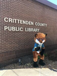 A mascot is standing in front of the crittenden county public library.