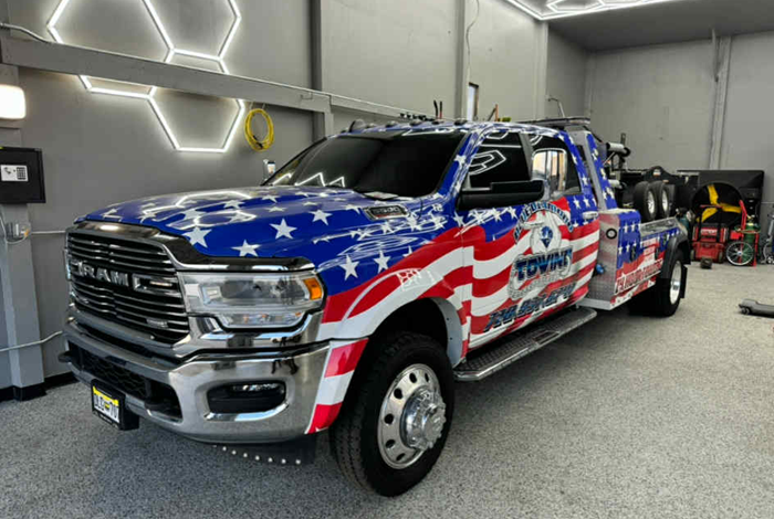 Tow truck with American flag design, inside a garage with fluorescent honeycomb lights.