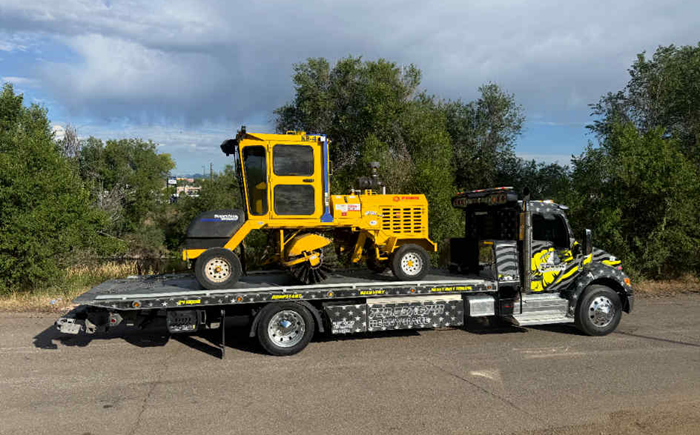 Yellow street sweeper on a flatbed tow truck outdoors on a sunny day.