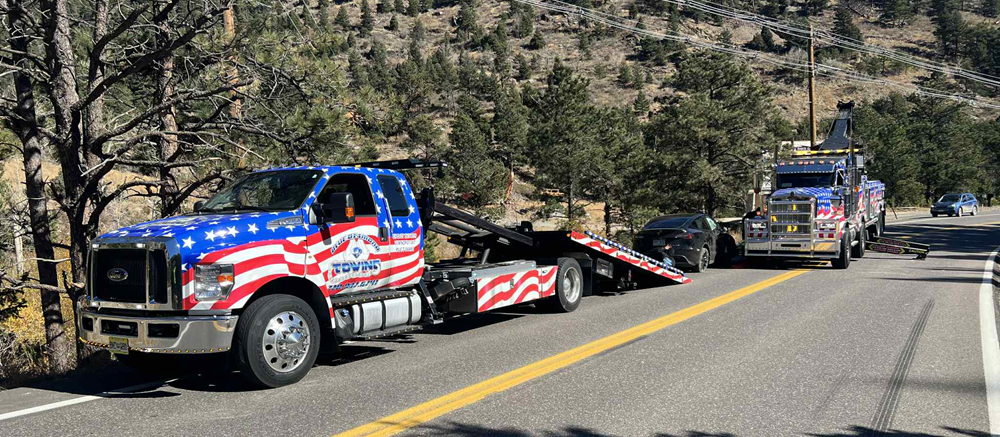 Tow trucks on a road with a vehicle being loaded; American flag design on the trucks.