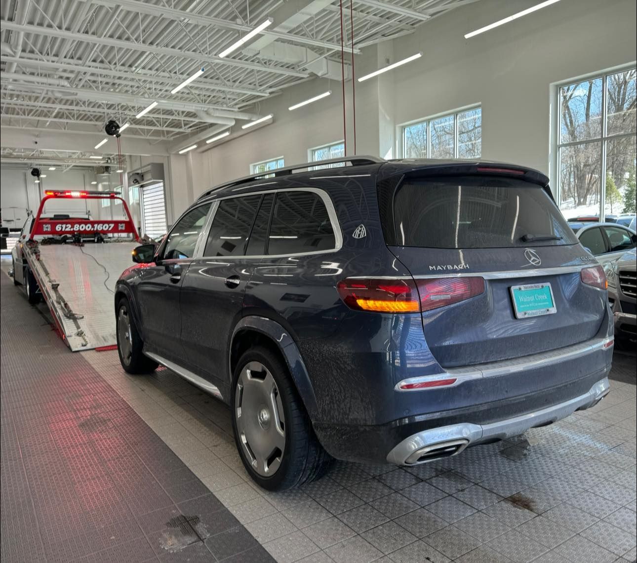 Dark blue Maybach SUV parked inside, being towed by a red tow truck. Brightly lit garage.