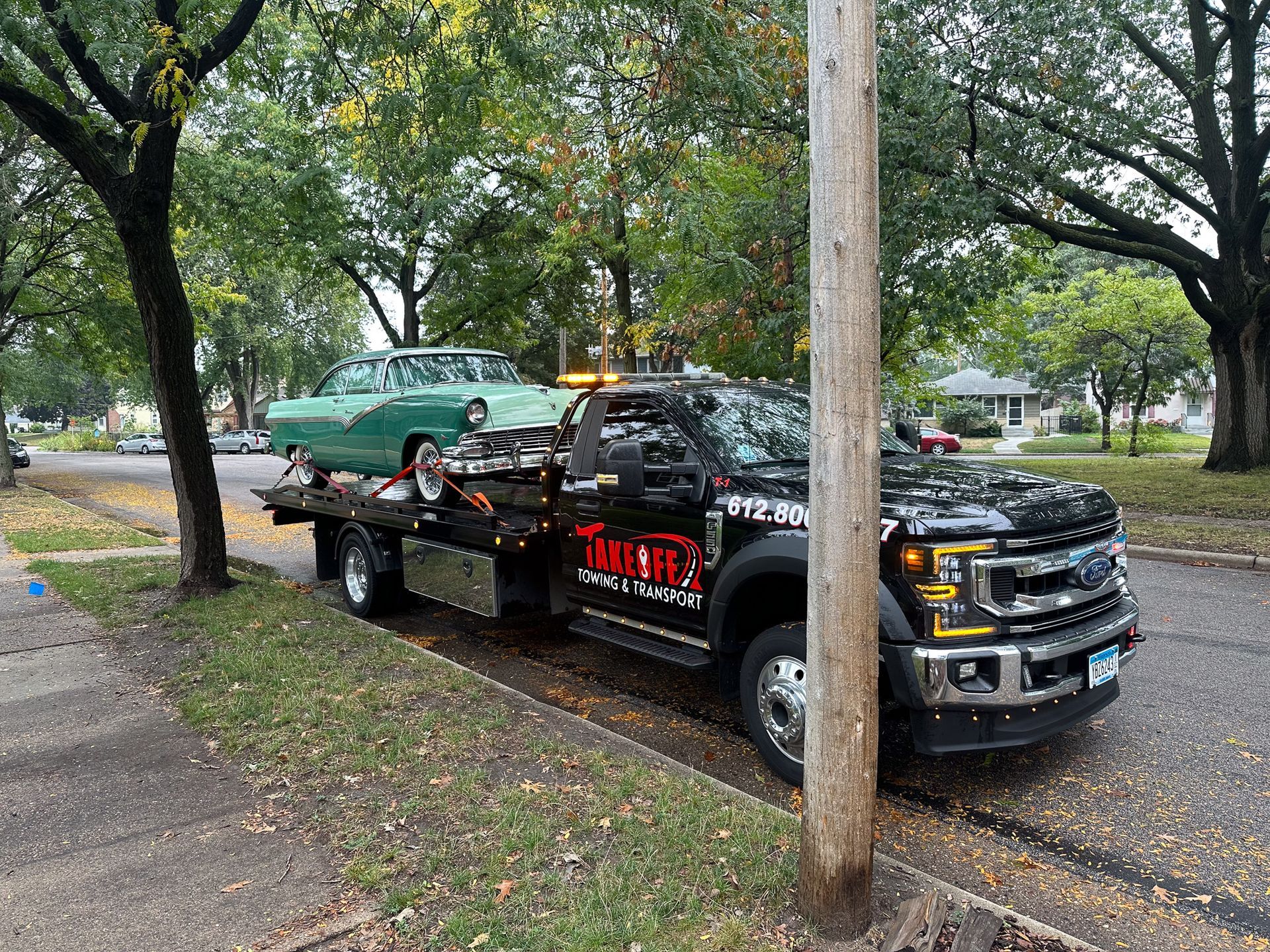 A classic green car on a tow truck parked on a city street.