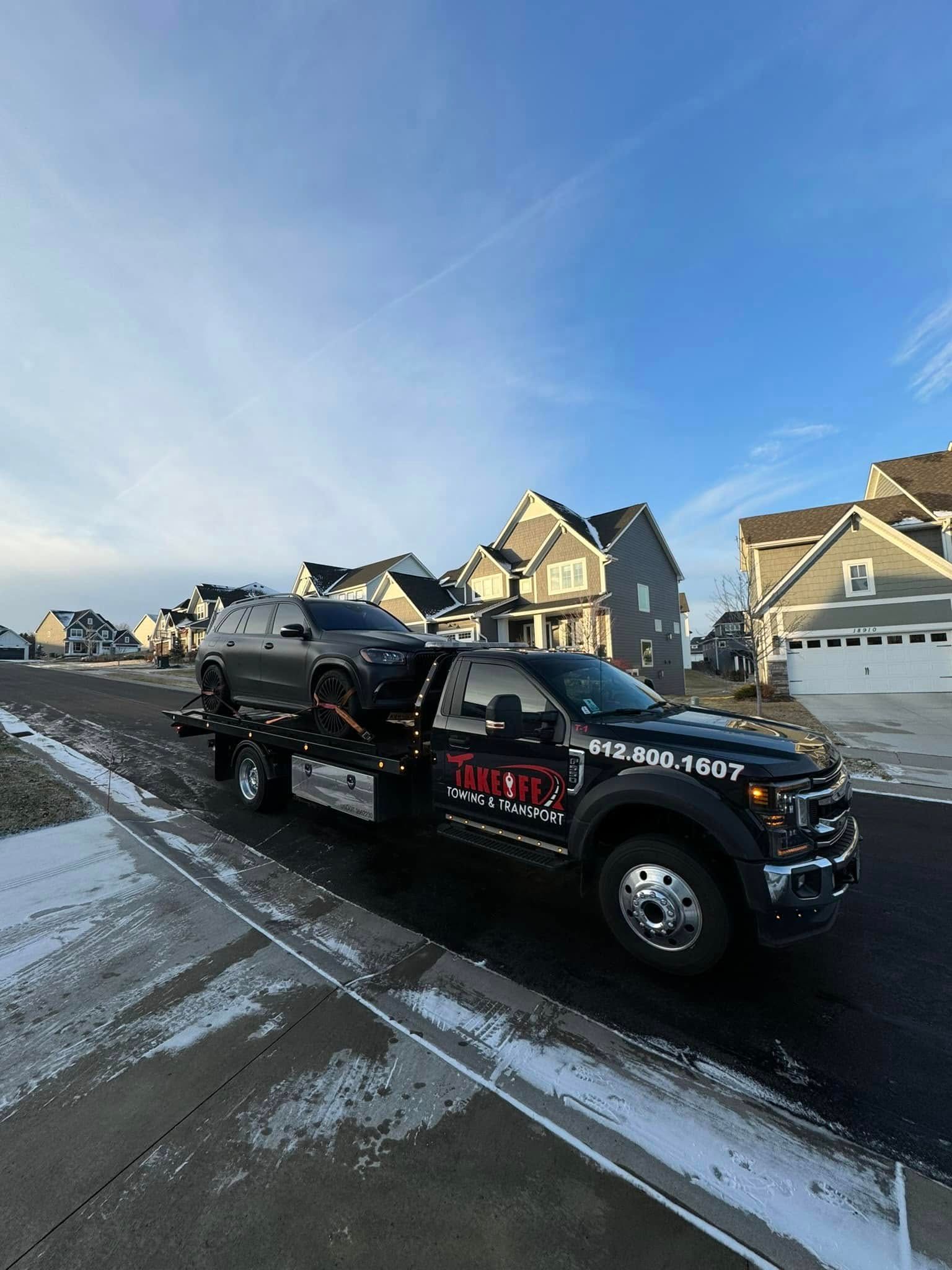 Tow truck carrying a car on a residential street under a blue sky.