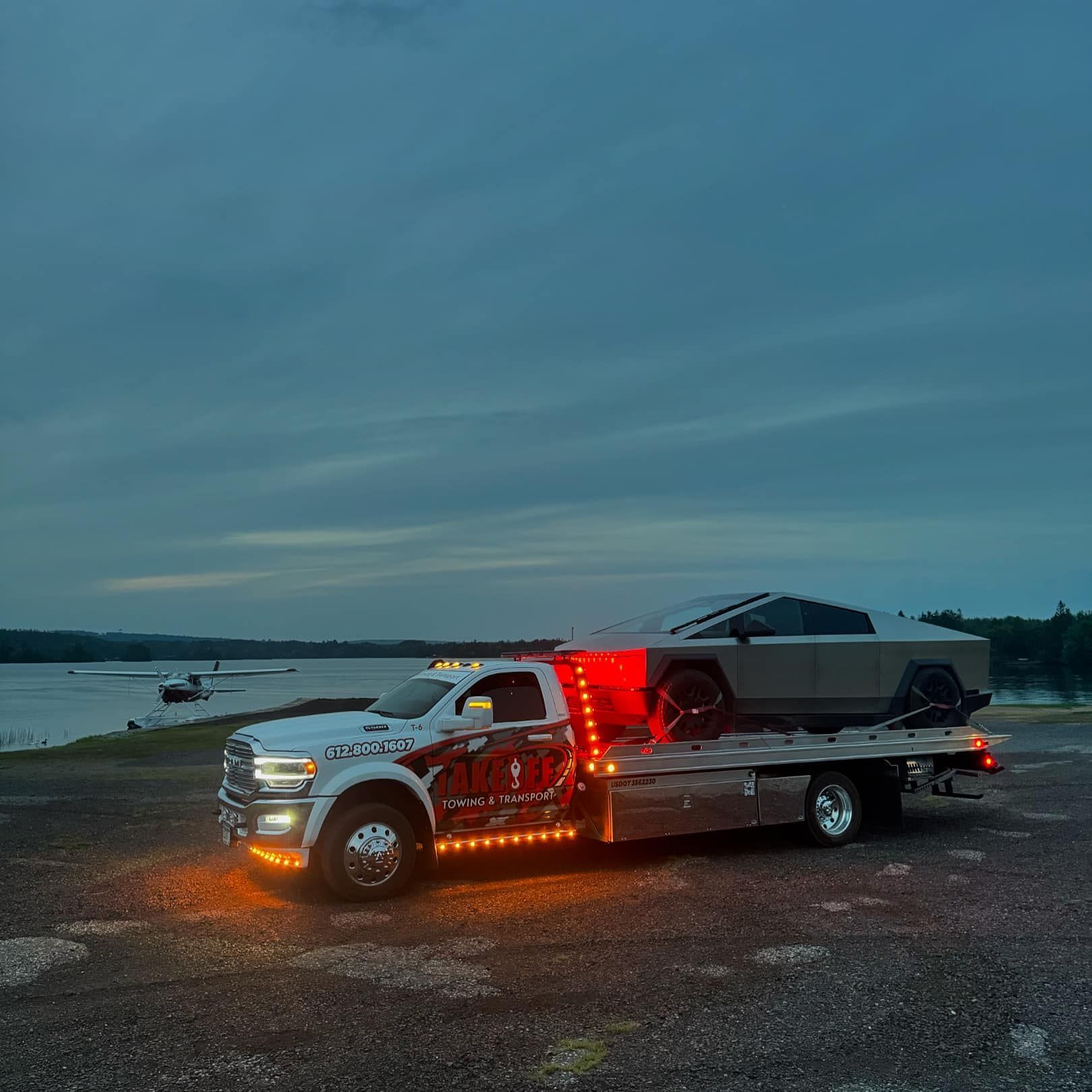A Tesla Cybertruck loaded on a tow truck at dusk near a body of water.
