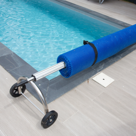 a blue solar blanket is rolled up next to a swimming pool .