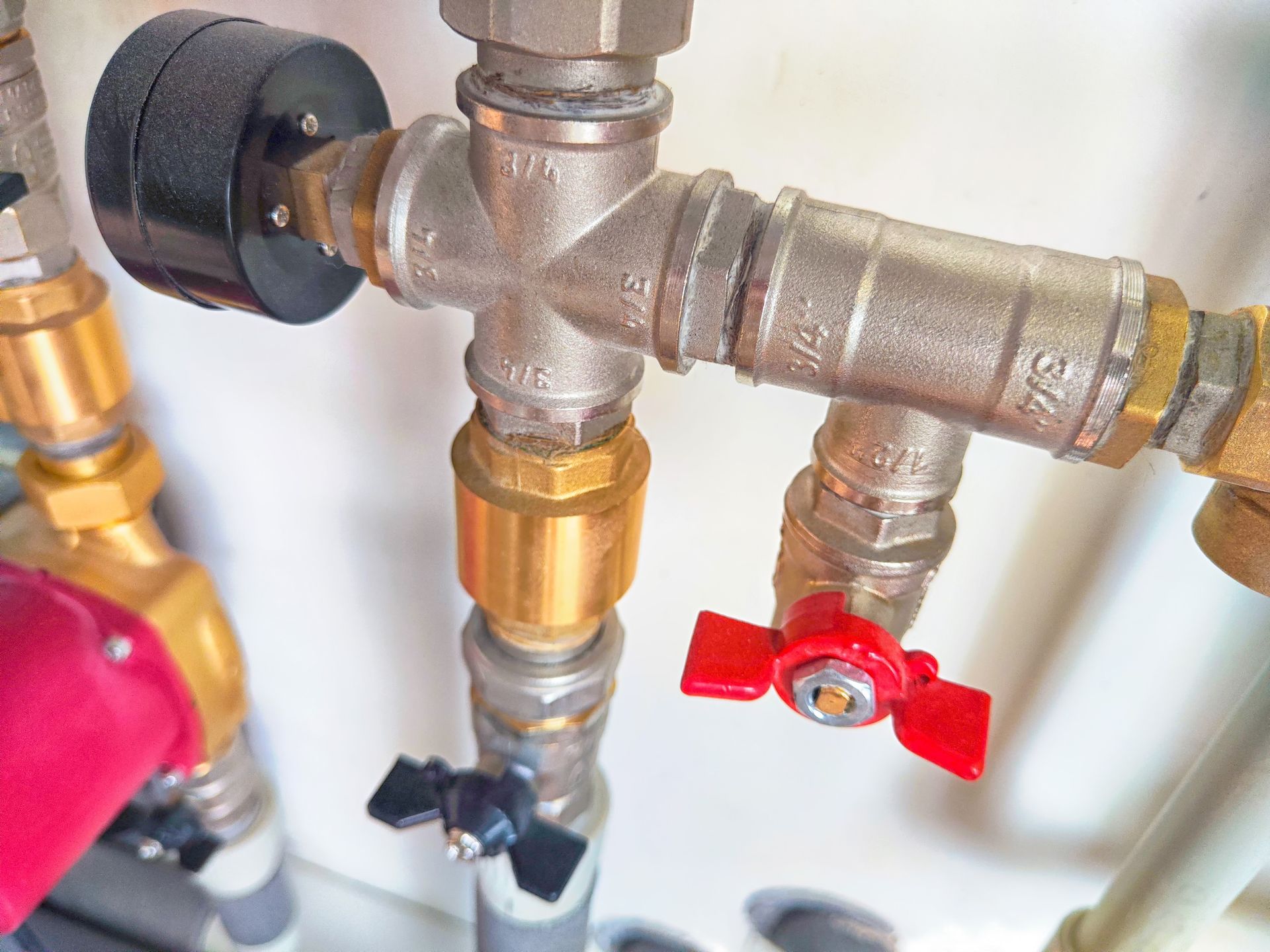 Close-up of plumbing pipes with a pressure gauge and red and black valve handles.