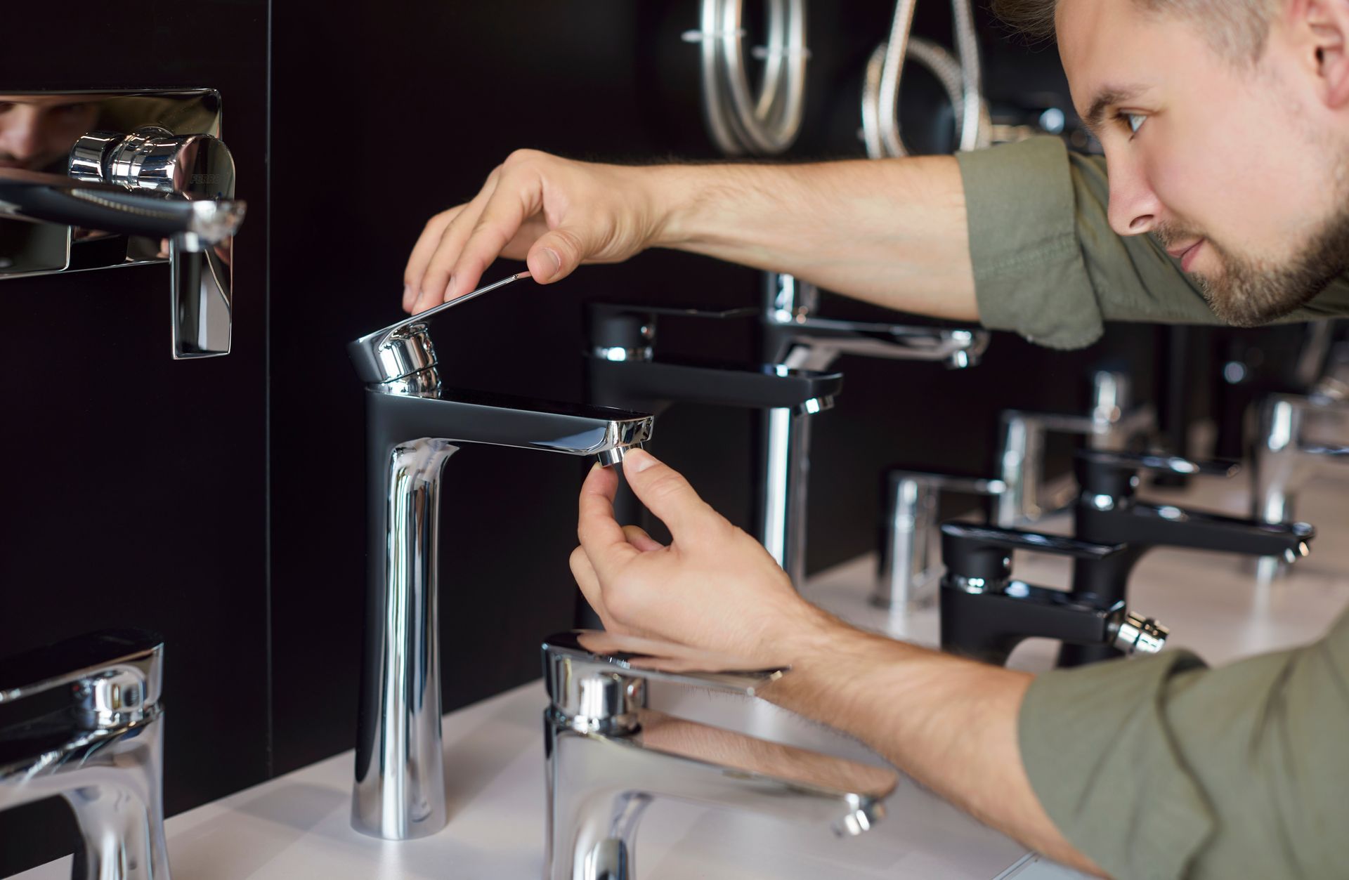 Man examining a chrome faucet display in a store; black background.