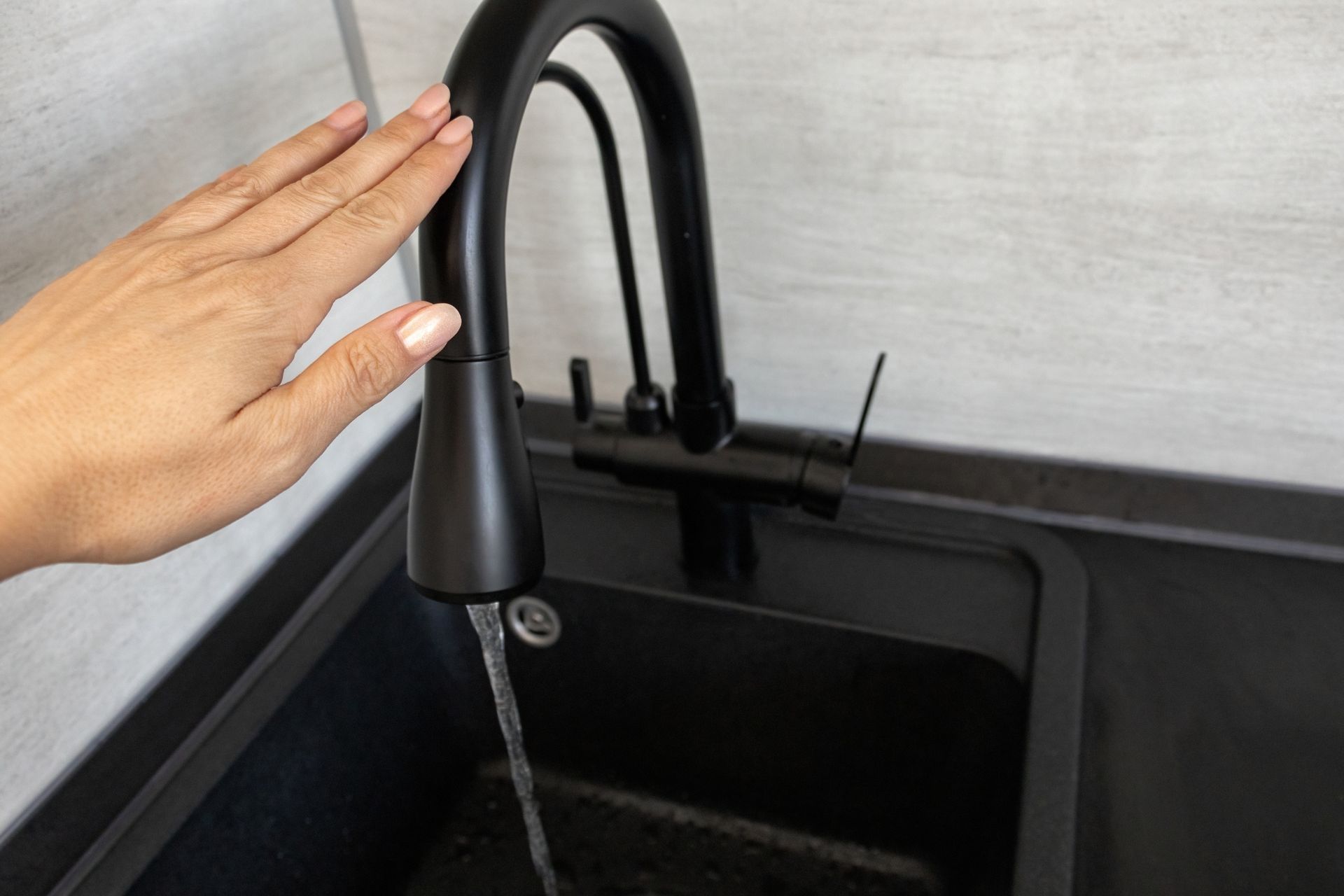 Black kitchen faucet with a hand near it, water flowing into a black sink.