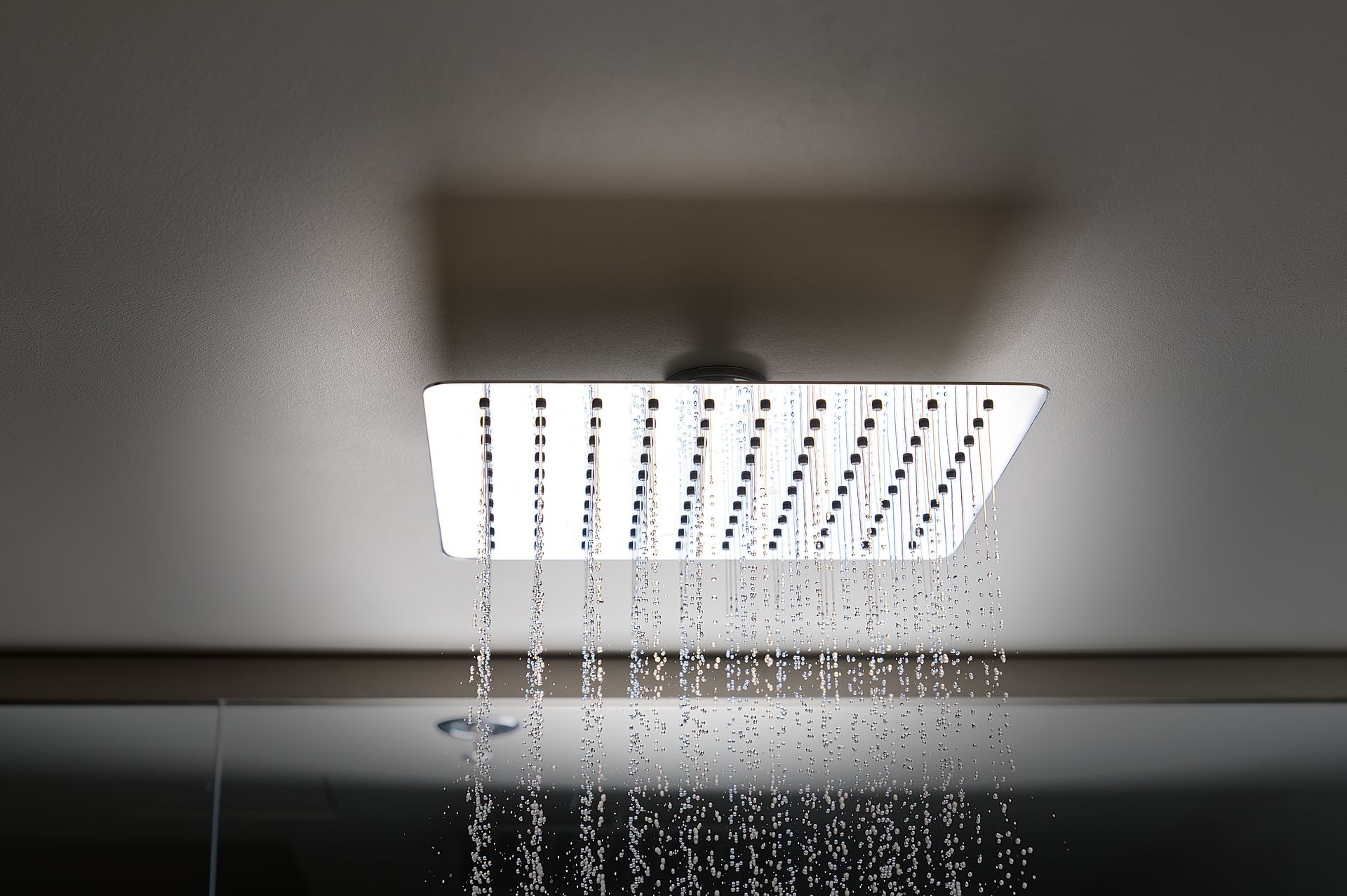 Square showerhead with water droplets falling in front of a white ceiling.