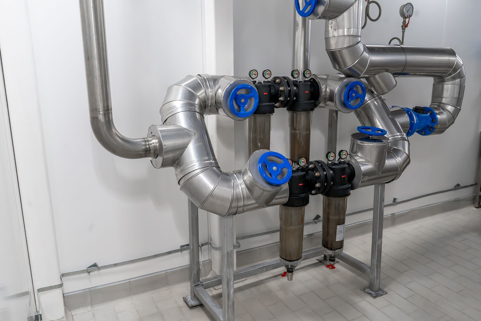 A row of stainless steel pipes with blue valves in a room.