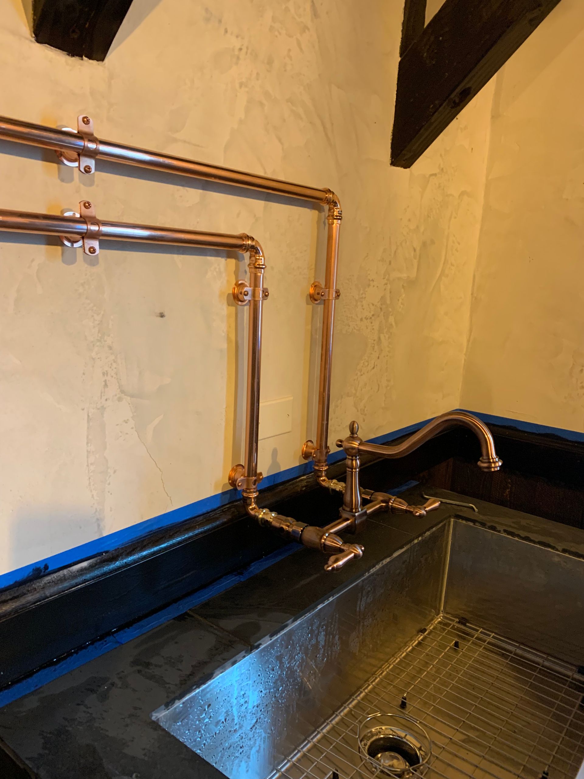 A kitchen sink with copper pipes hanging from the wall.