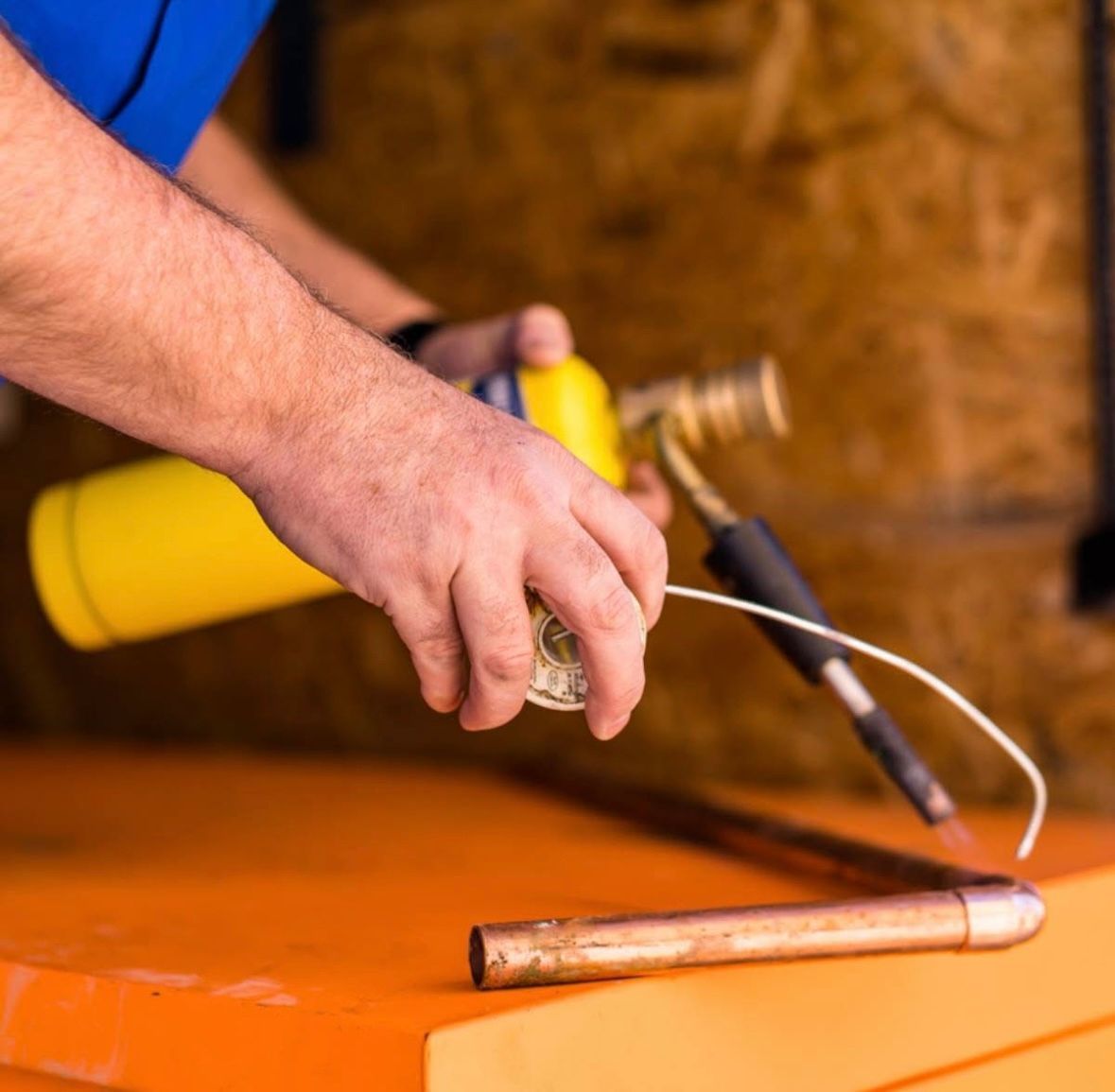 A man is using a torch to heat a copper pipe