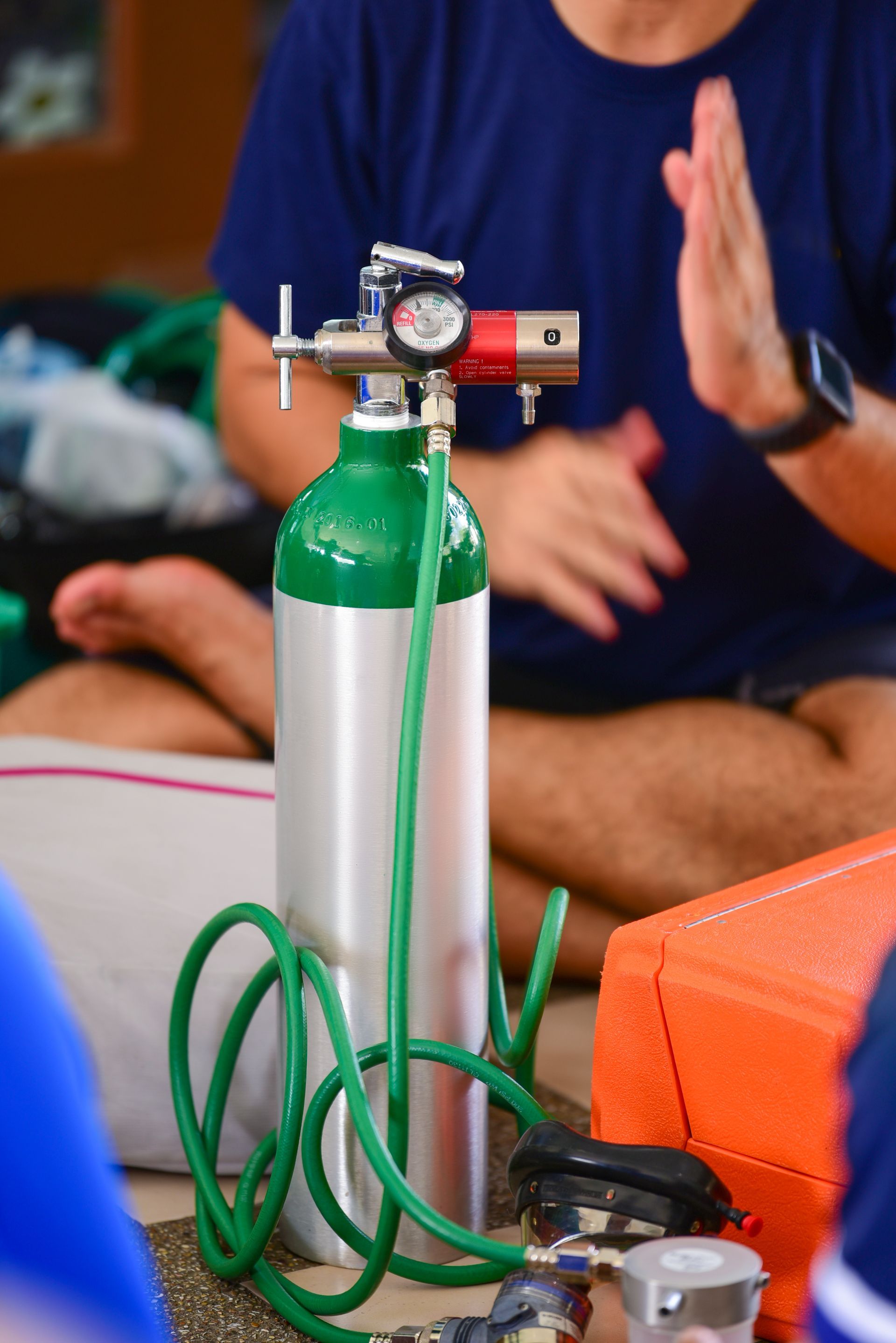 A man is sitting on the floor next to an oxygen cylinder.