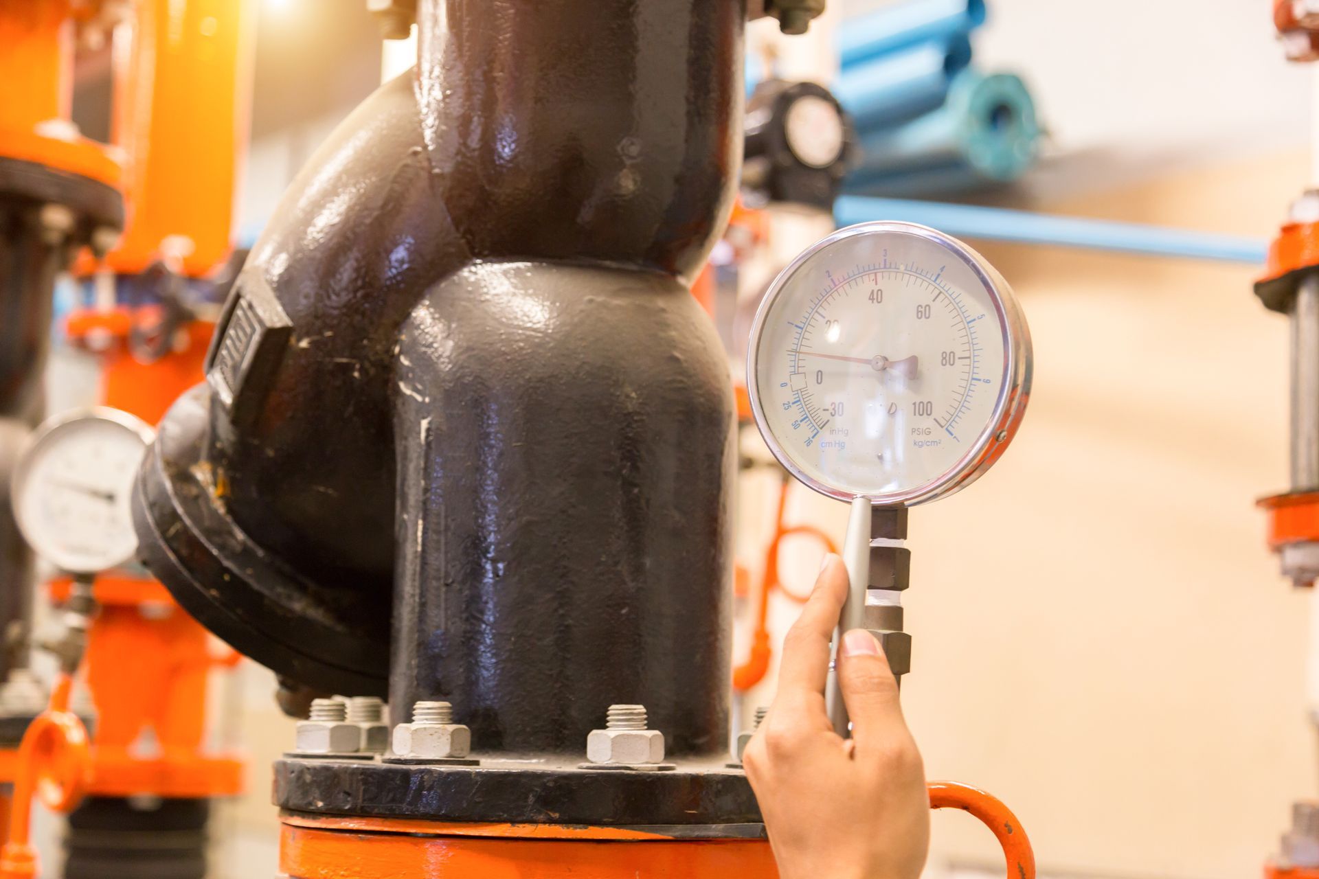 A person is holding a pressure gauge next to a pipe in a factory.