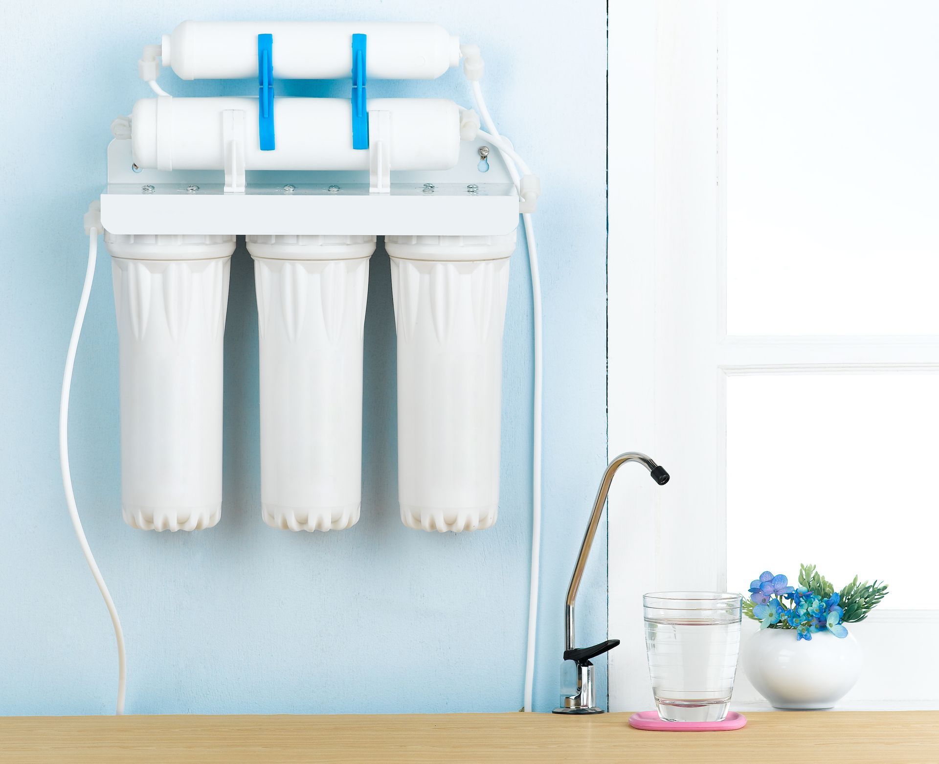A water filter is hanging on a wall next to a glass of water.