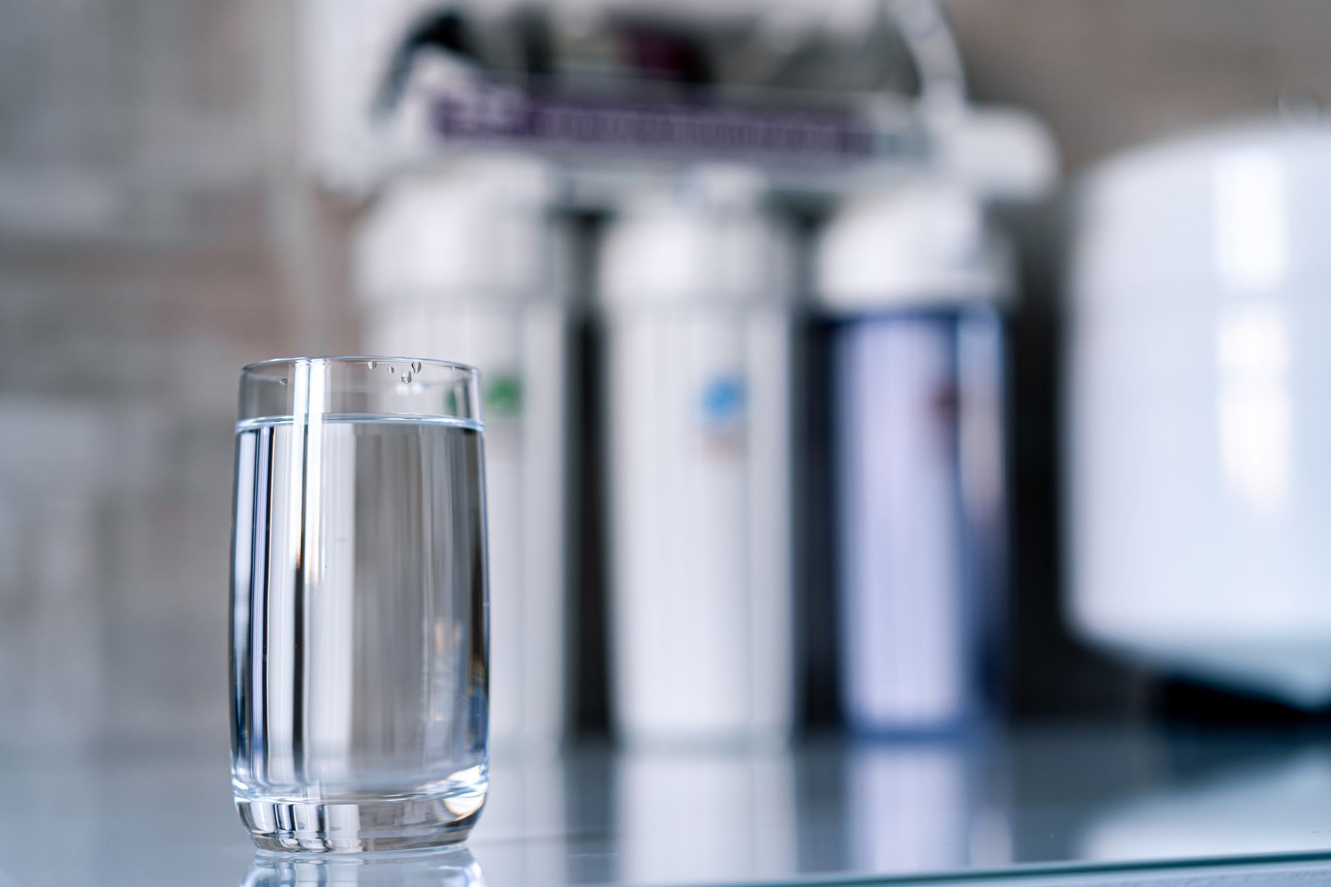 A glass of water is sitting on a glass table in front of a water filter.