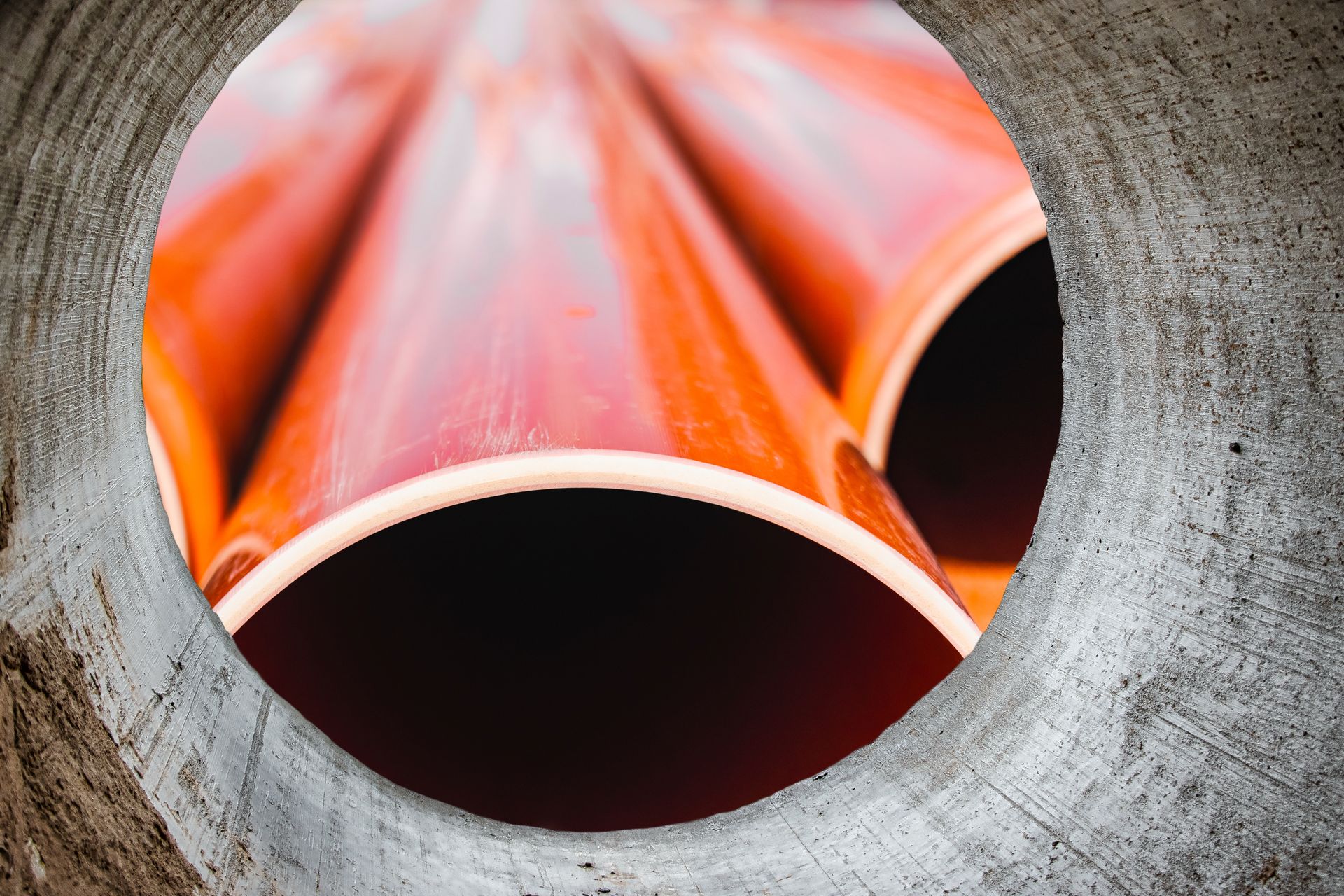 A close up of a hole in a concrete wall with orange pipes coming out of it.