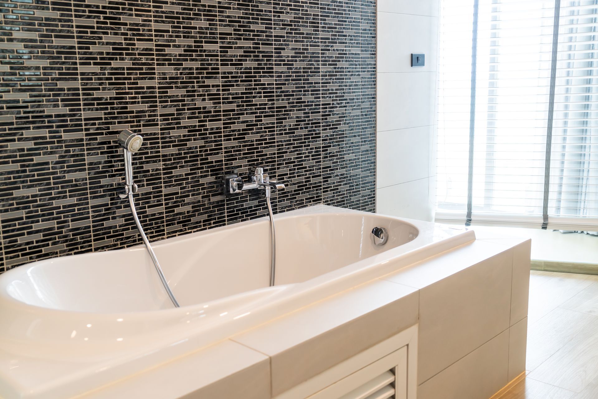 A bathtub with a shower head in a bathroom next to a window.