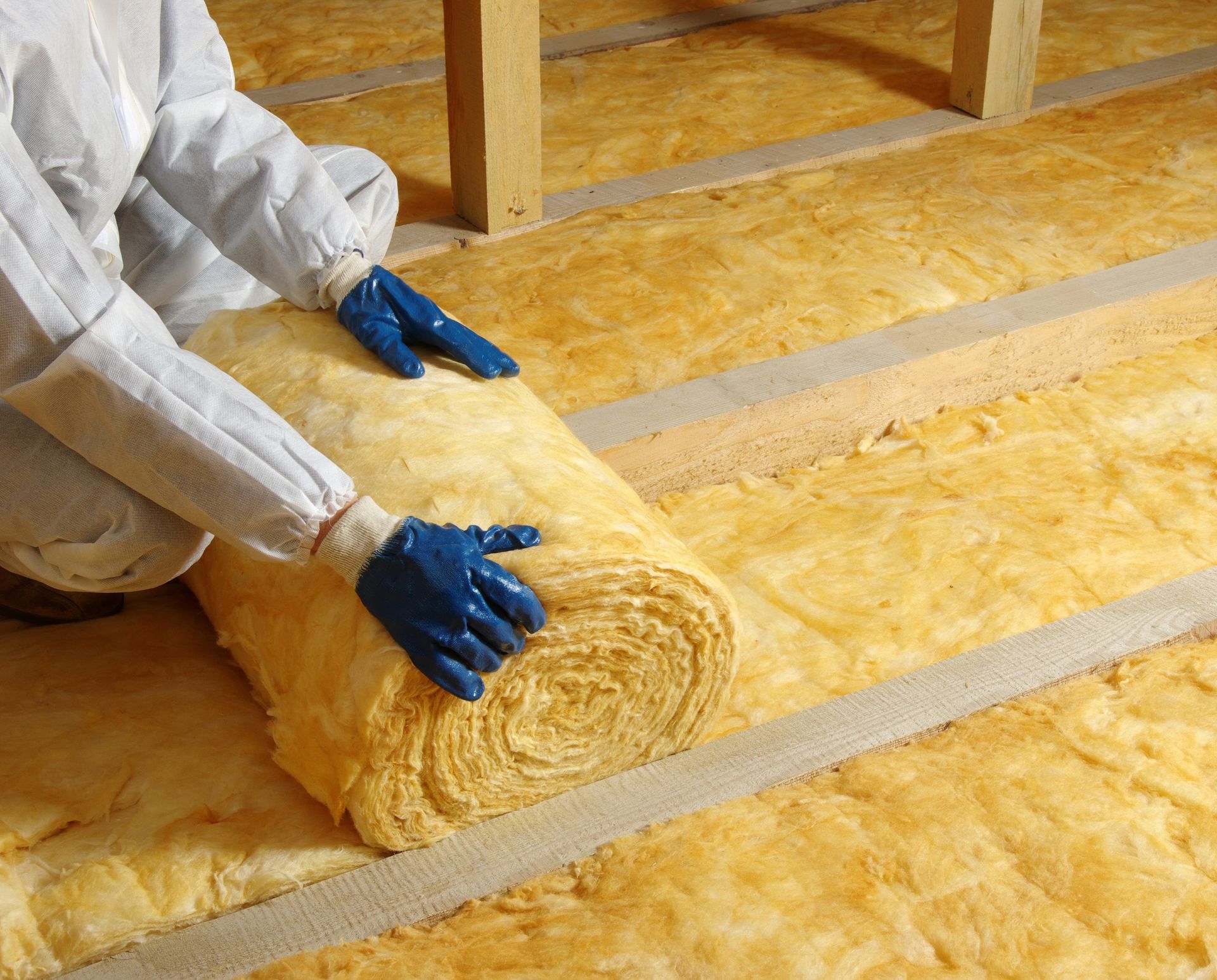 A person is laying a roll of insulation on the floor.