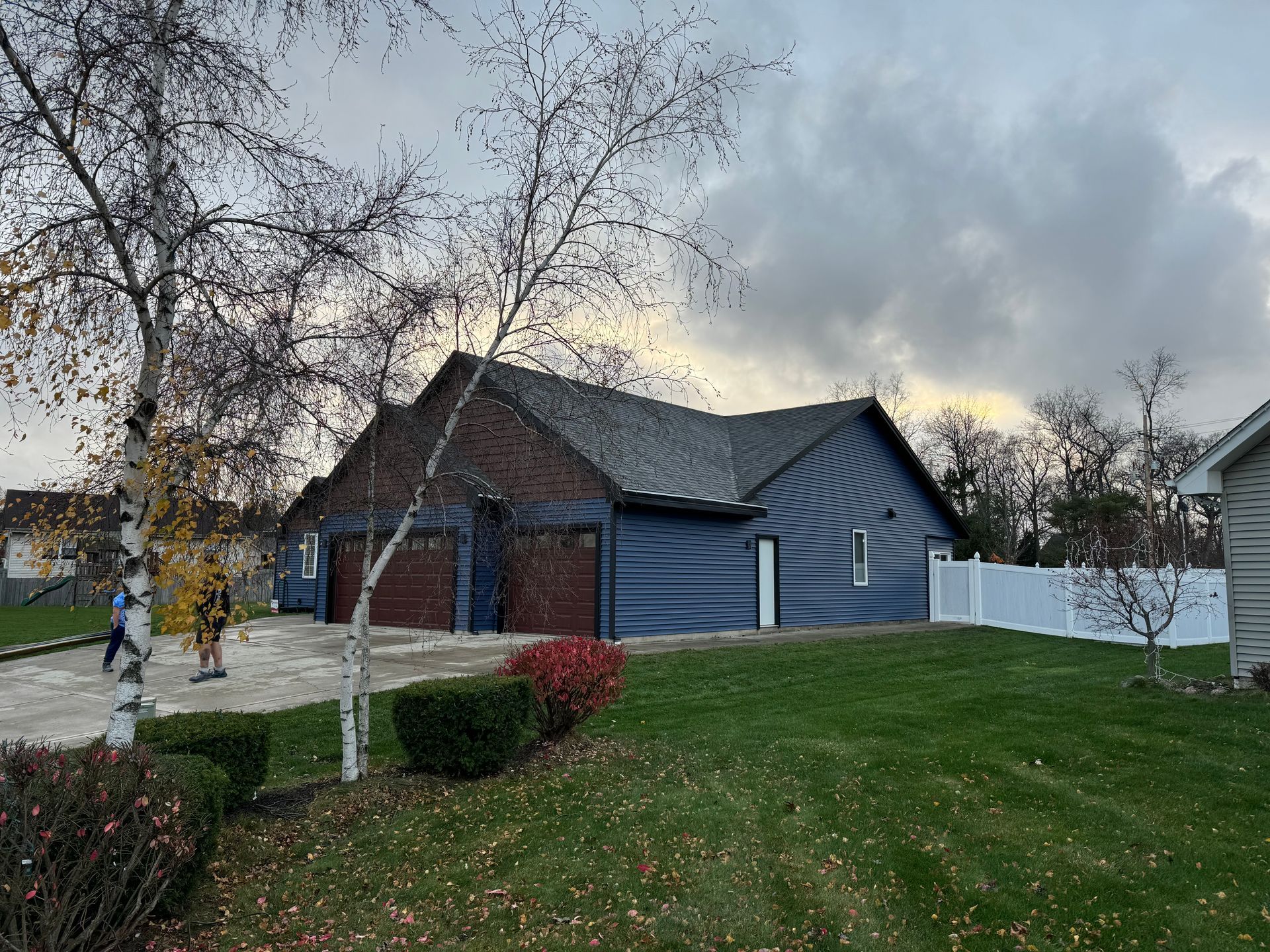 Blue house with a three-car garage, red doors, and a green lawn under a cloudy sky.