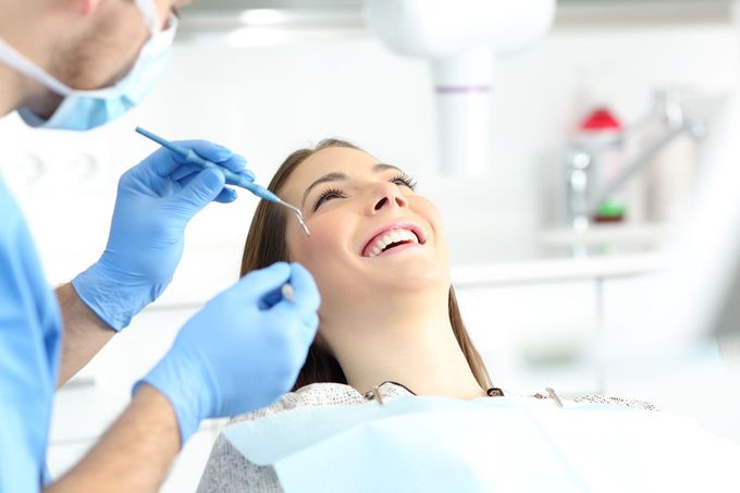 Un dentista con i guanti blu cura un paziente sorridente in una luminosa clinica odontoiatrica.