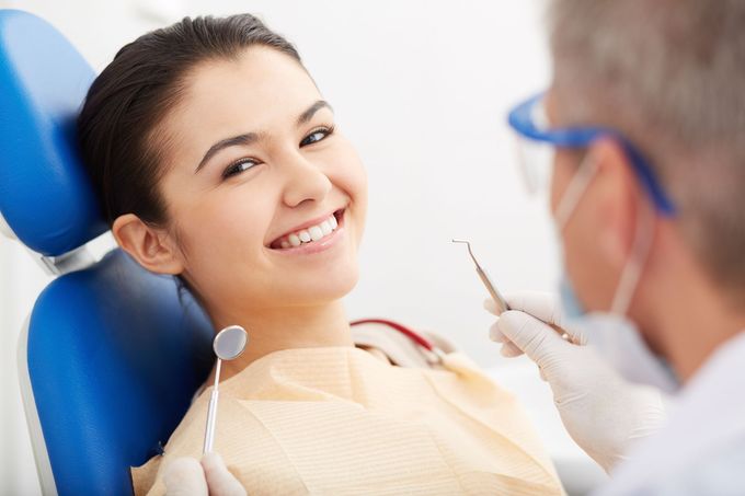 Paziente sorridente sulla poltrona odontoiatrica mentre il dentista prepara uno strumento durante una visita di controllo.