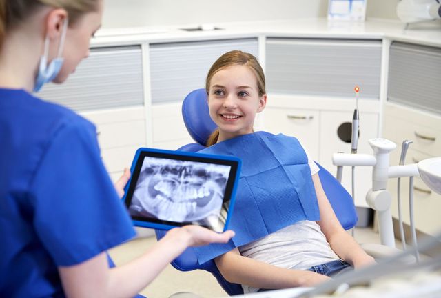 Il dentista mostra una radiografia su un tablet a un paziente sorridente seduto sulla poltrona odontoiatrica.